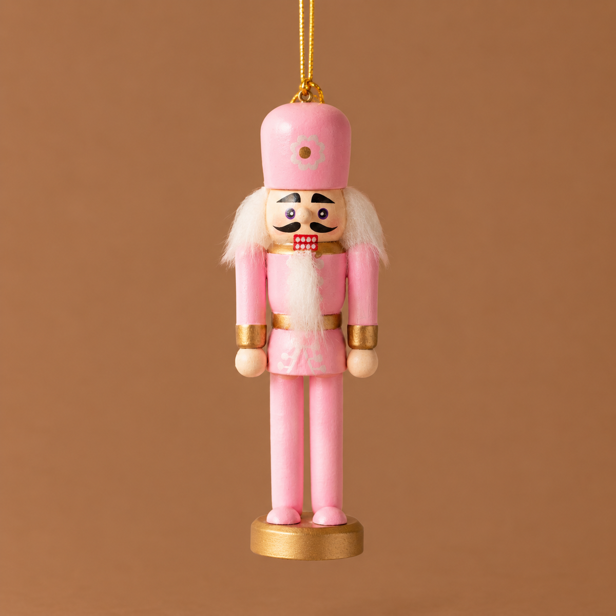 A pink wooden nutcracker figure with a tall pink hat, white hair and beard, gold accents, and a gold round base, standing against a warm brown background.