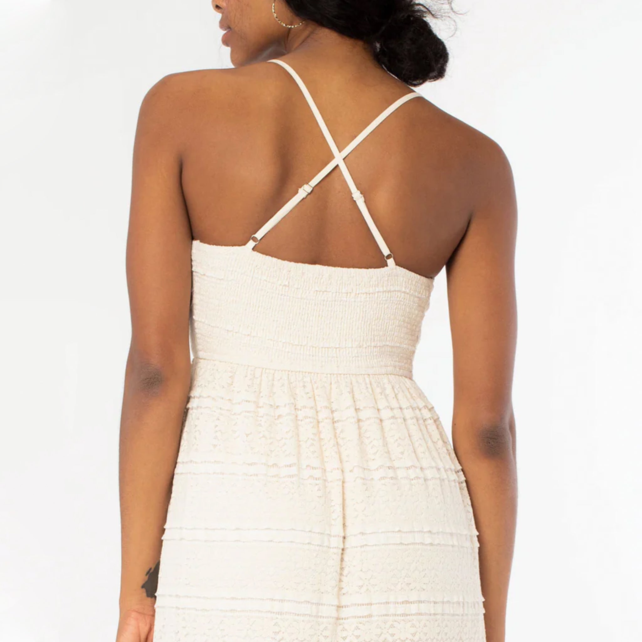 On a white background is a natural colored lace dress with spaghetti straps and a cross cross back.