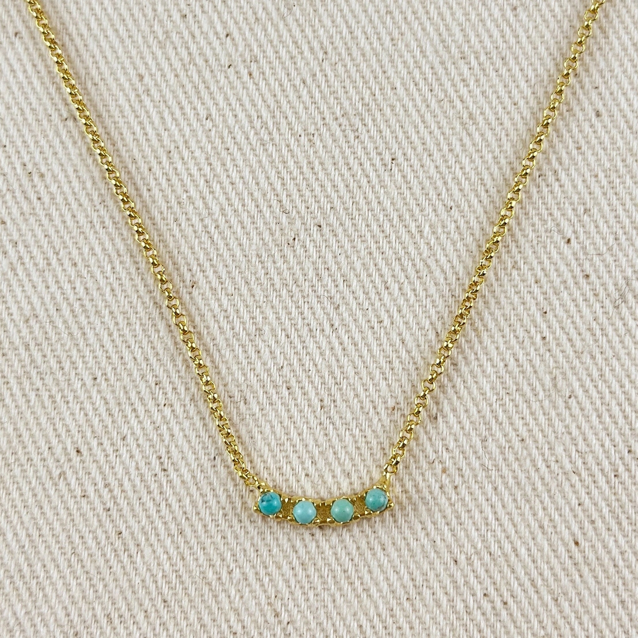 A gold chain necklace with a pendant that has four small turquoise beads on a horizontal gold bar. 