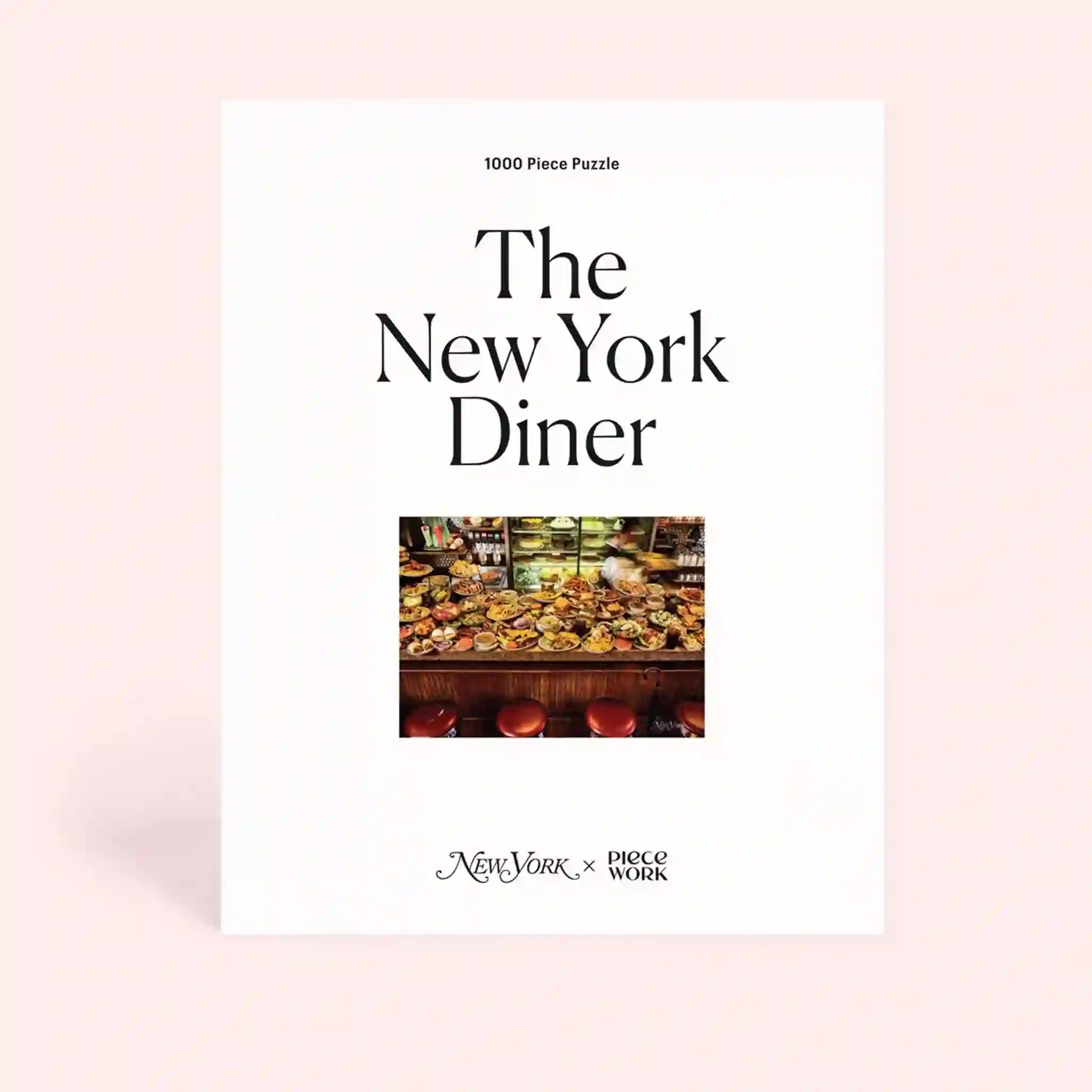 On a pink background is a white puzzle box with black text that reads, "The New York Diner" along with an image of diner food and a bar.