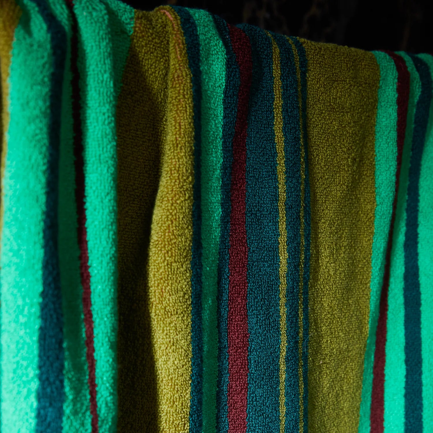 Close-up of a textured towel with vertical stripes in teal, olive green, and burgundy.