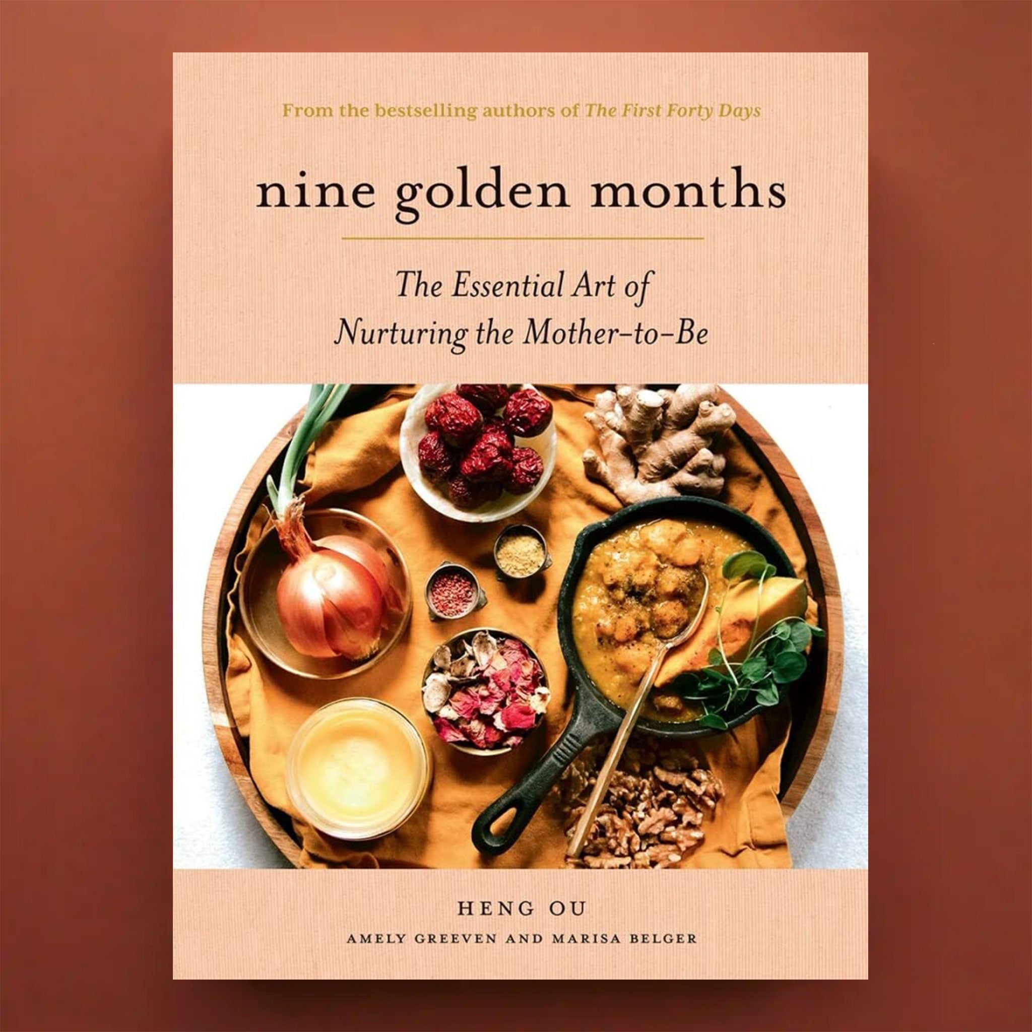 On a brown background is a book with a plate of food and the title at the top that reads, "nine golden months", "The Essential Art of Nurturing the Mother-to-Be".