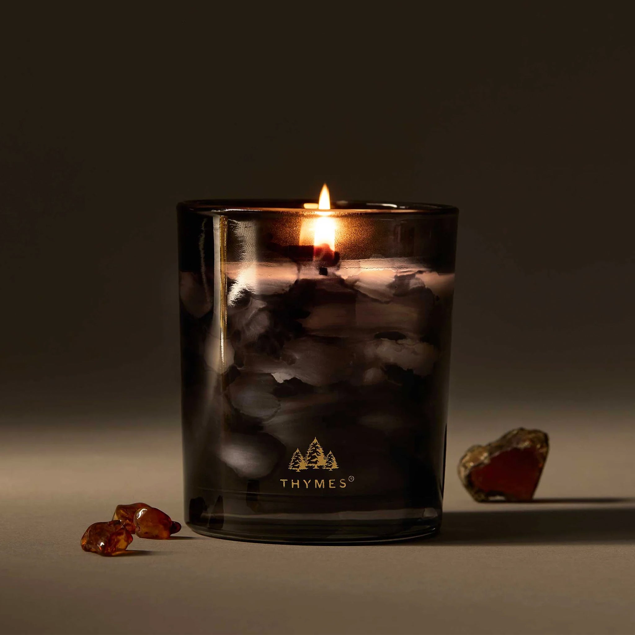 A black jarred candle with white wax and gold foiled text that reads, 'Thymes'. 