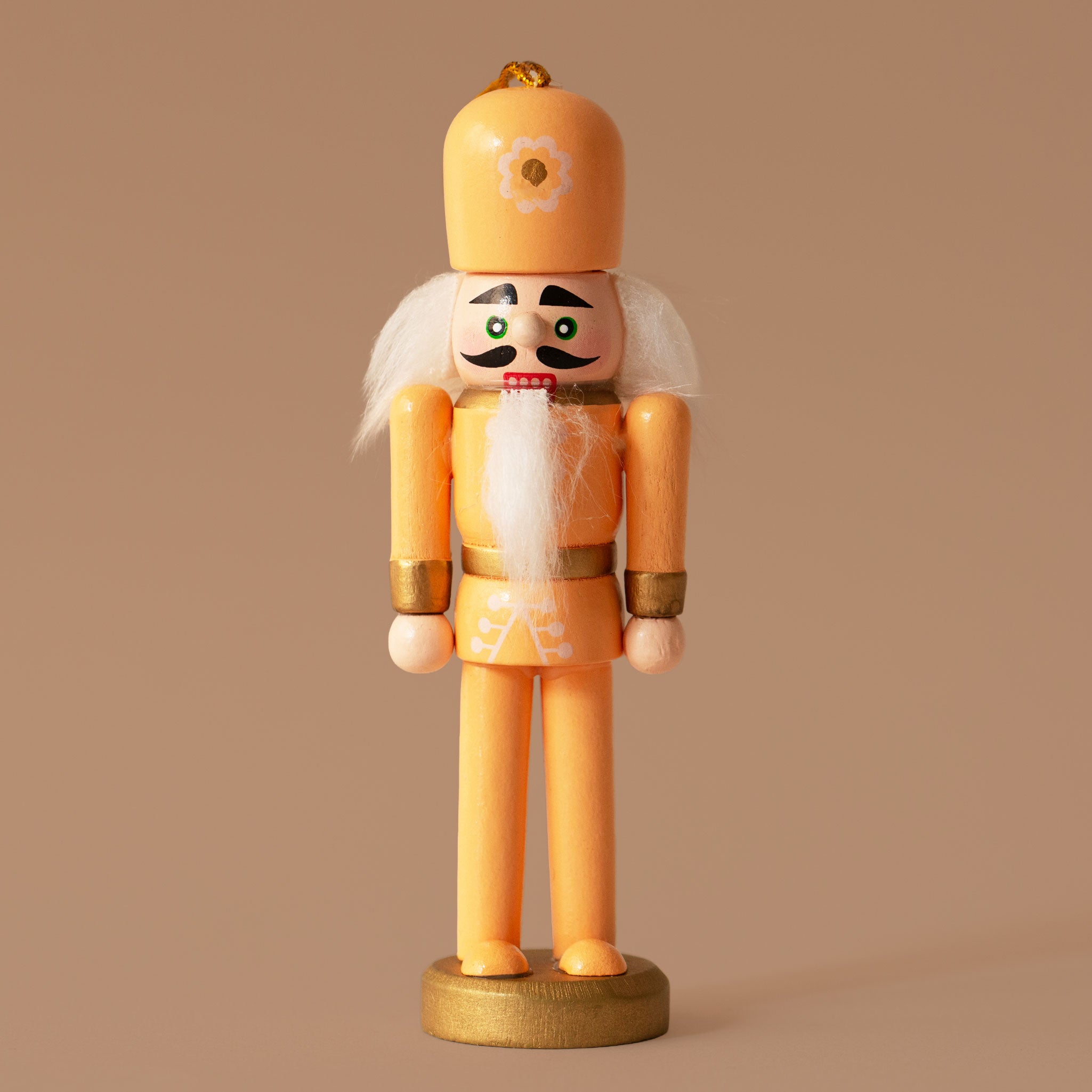 An orange wooden nutcracker figure with a tall pink hat, white hair and beard, gold accents, and a gold round base, standing against a warm brown background