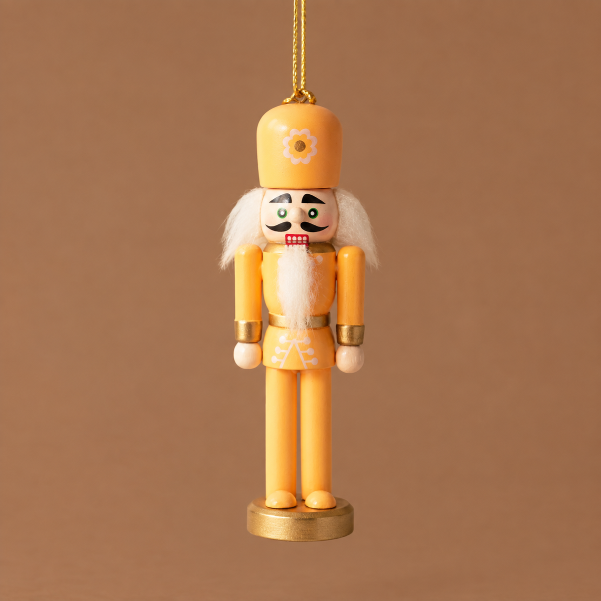 An orange wooden nutcracker figure with a tall pink hat, white hair and beard, gold accents, and a gold round base, standing against a warm brown background