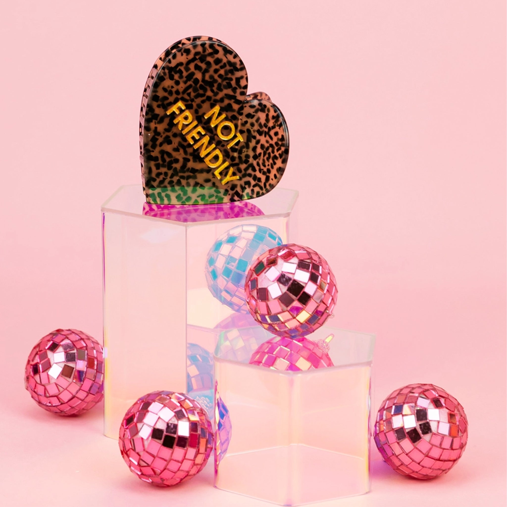 A heart shaped black and brown hair clip with gold text that reads, "Not Friendly". 