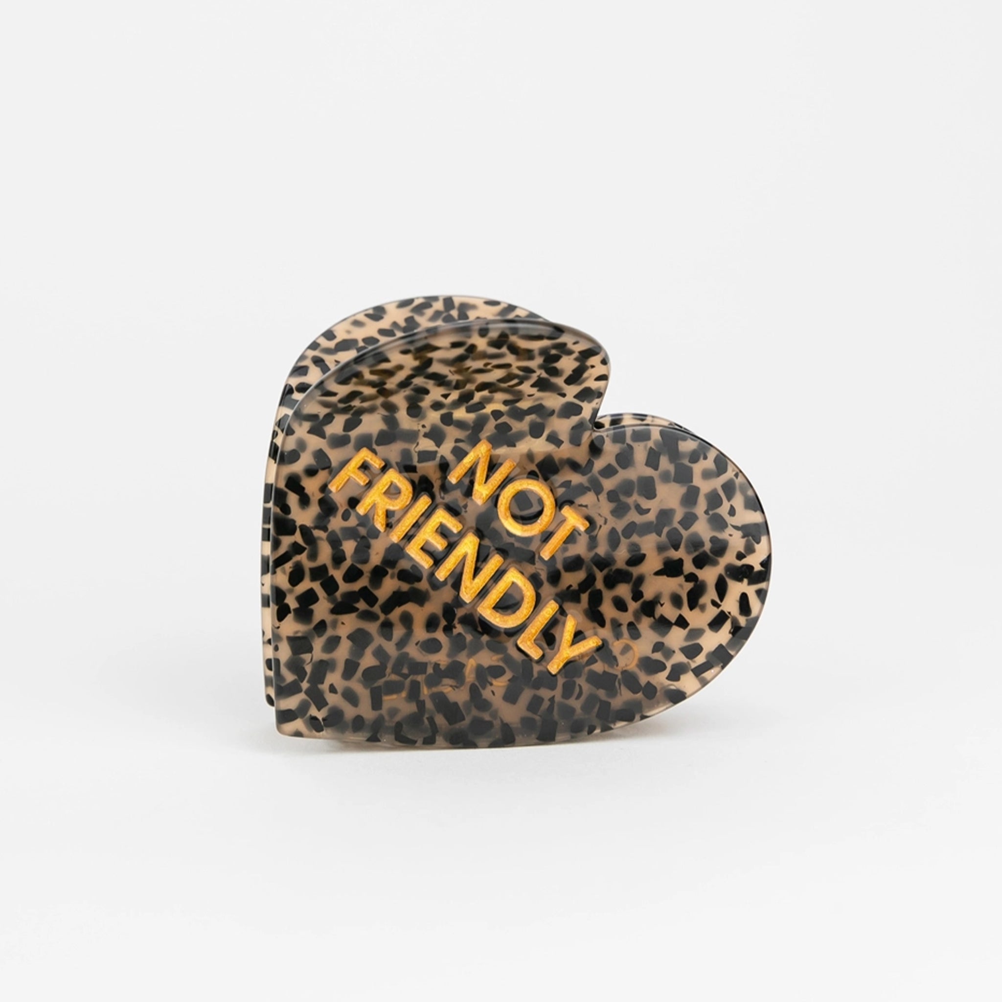 A heart shaped black and brown hair clip with gold text that reads, "Not Friendly". 