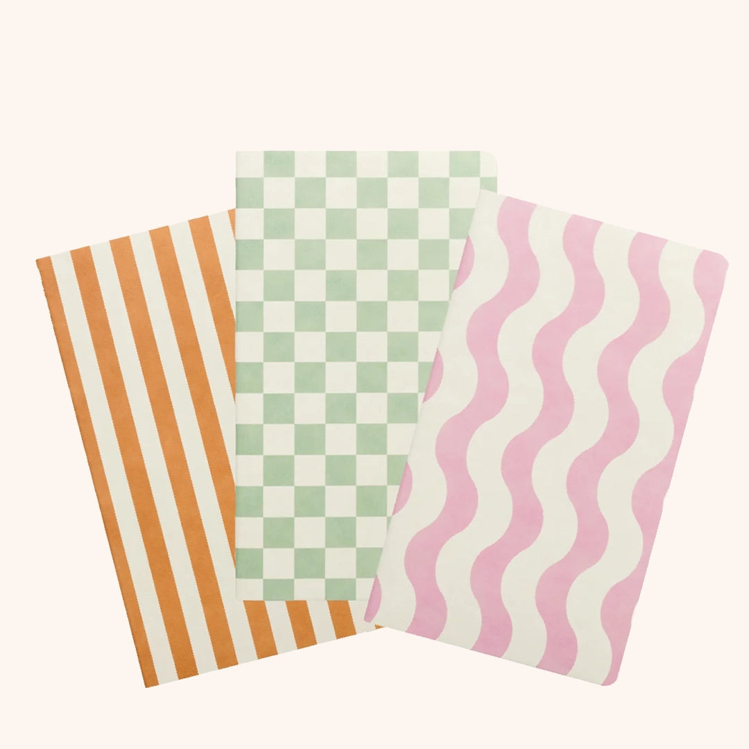 On a white background is a set of three notebooks featuring an orange and white stripe notebook, a green and white pattern and a pink and white wavy stripe design. 