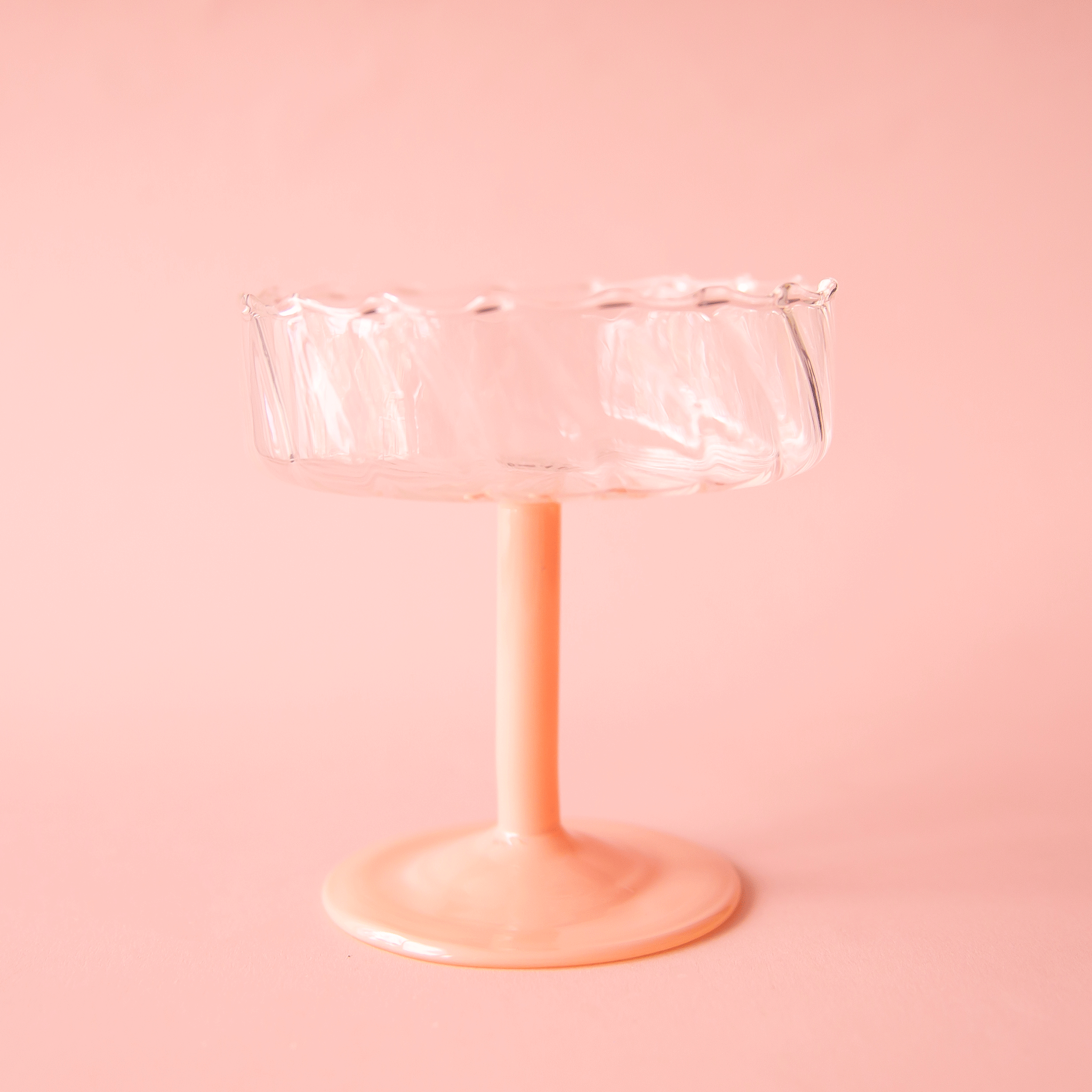 On a pink background is a wavy glass coupe with a pink stem.