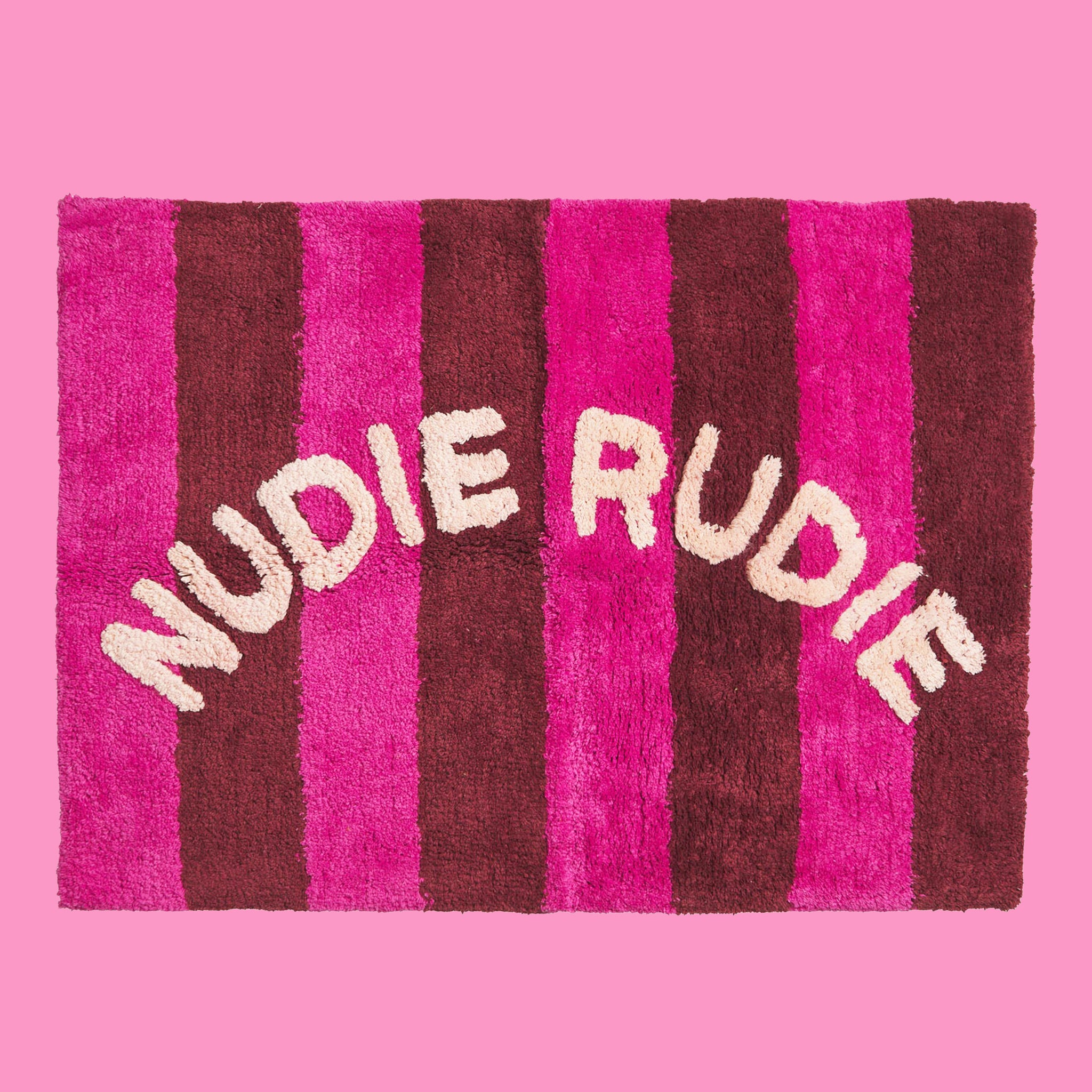 A hot pink and burgundy striped bath mat with white text arched in the center that reads, &quot;Nudie Rudie&quot;. 