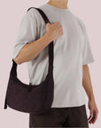 A purple/brownish colored nylon crescent bag with a black strap and details. 