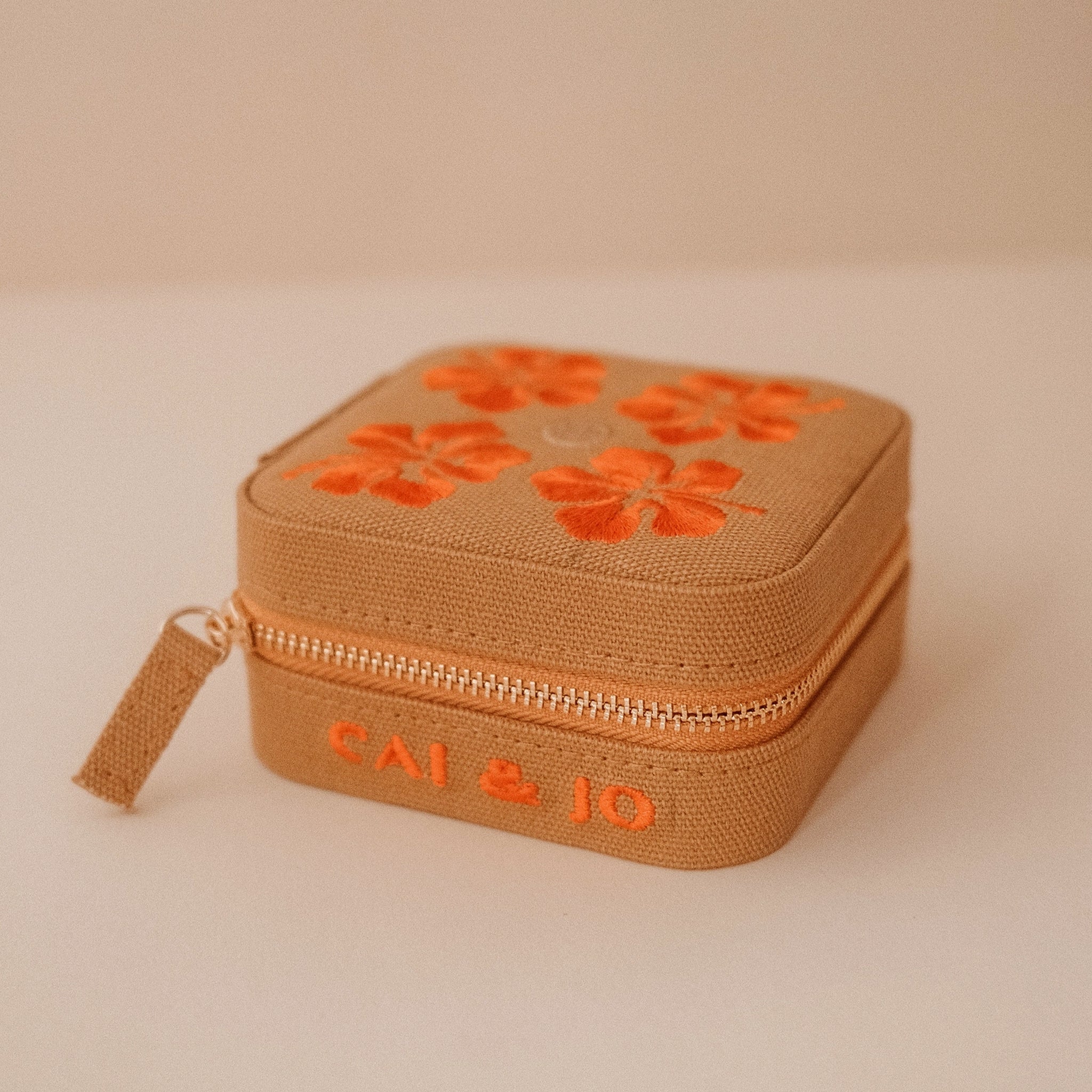 A tan jewelry case with orange flowers. 