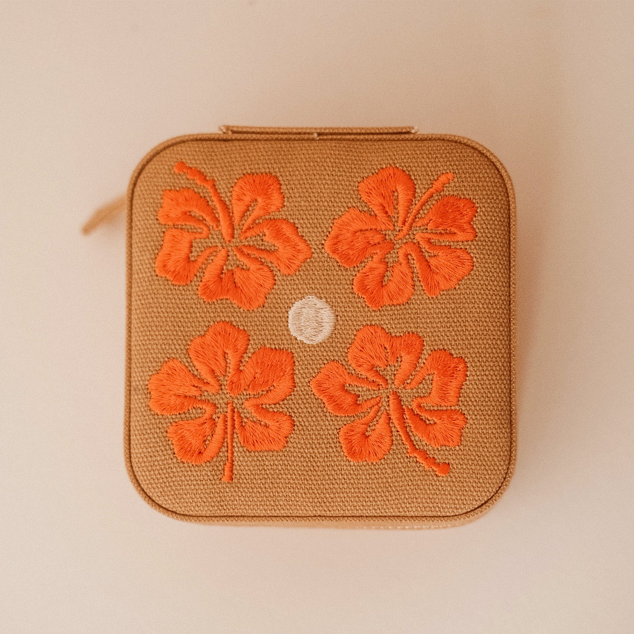 A tan jewelry case with orange flowers. 