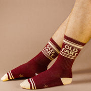 On a neutral is a model wearing a pair of dark red socks with ivory details and text at the top that reads, "Old Fart".