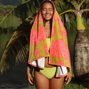 Woman in a green bikini with a floral towel draped over her shoulders, standing in a tropical setting.