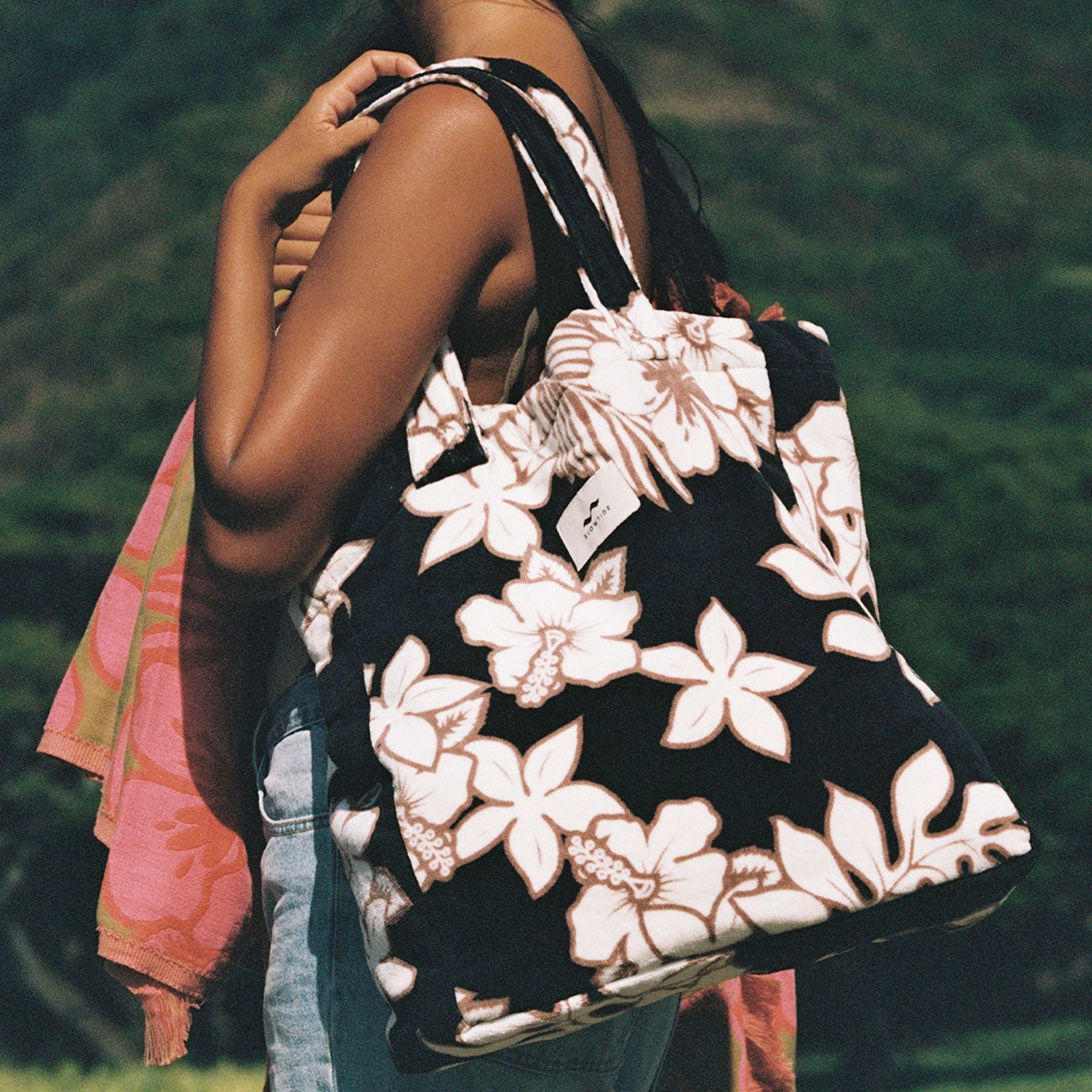 A black, cream and brown terry tote bag with a tropical floral print. 