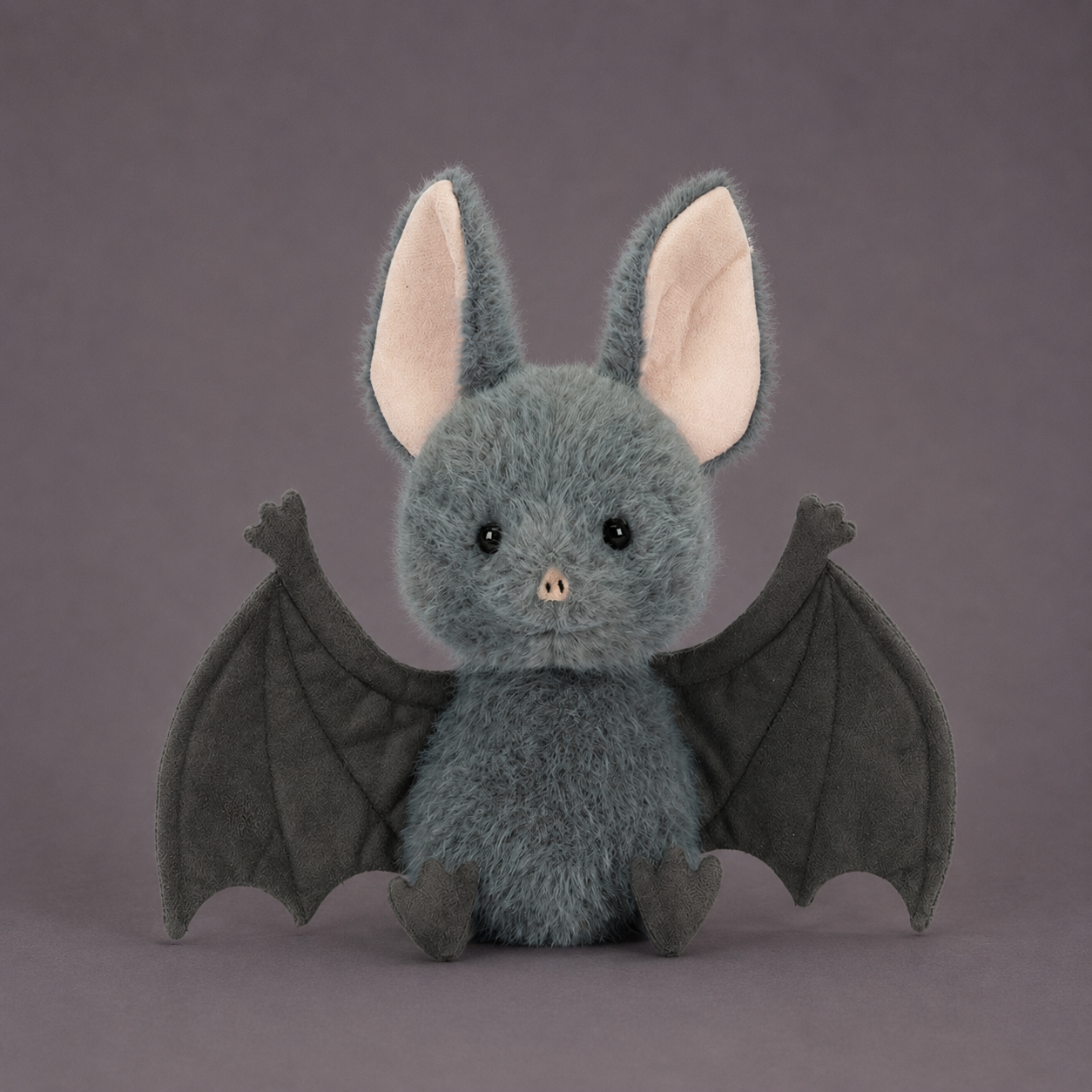 A grey bat shaped stuffed animal toy. 