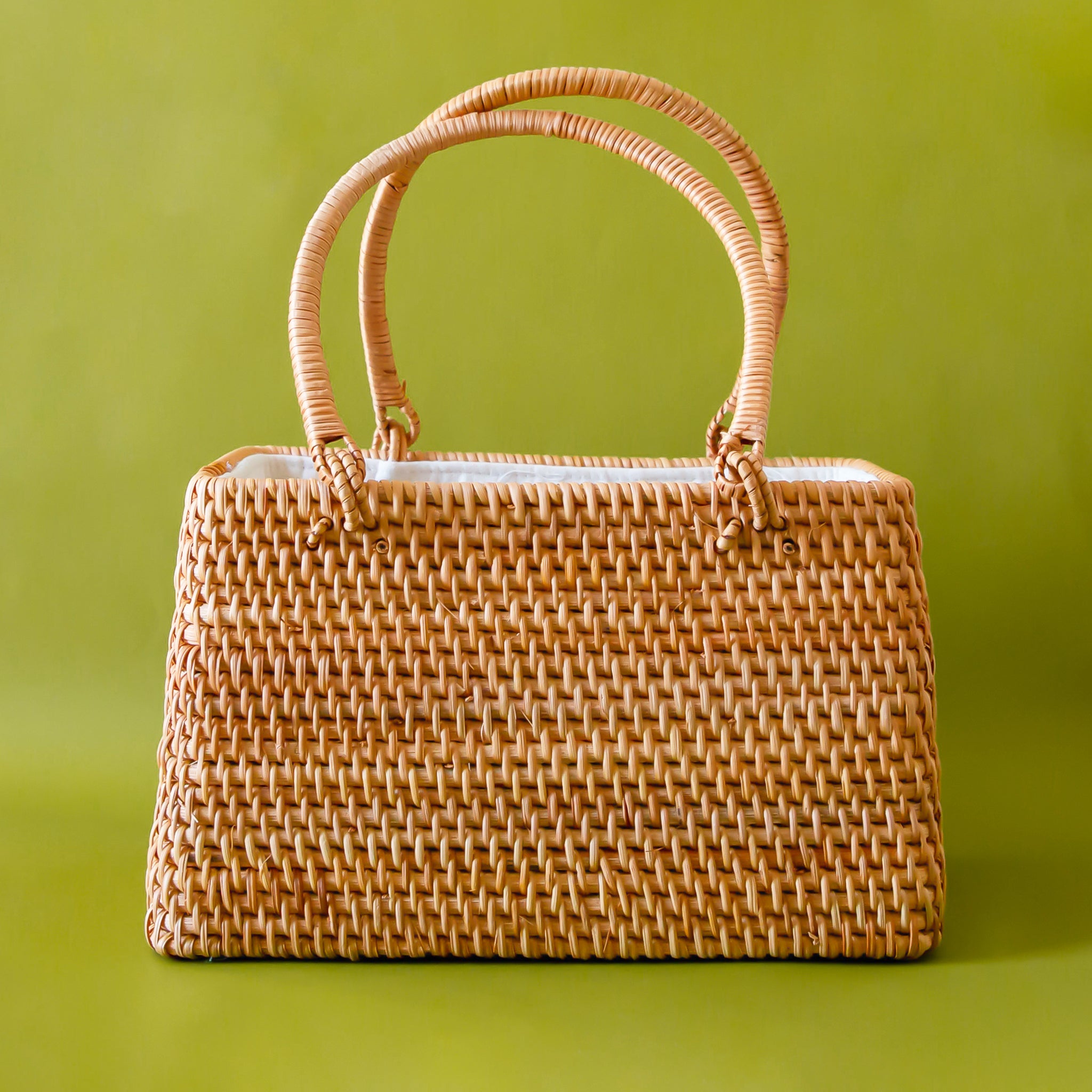 On a green background is a rattan handbag with two handles and a white lined interior. 