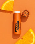 In front of white background is a bright orange tube with black text that reads ‘poppy & pout.’ On the far right side is the black outline of a flower.