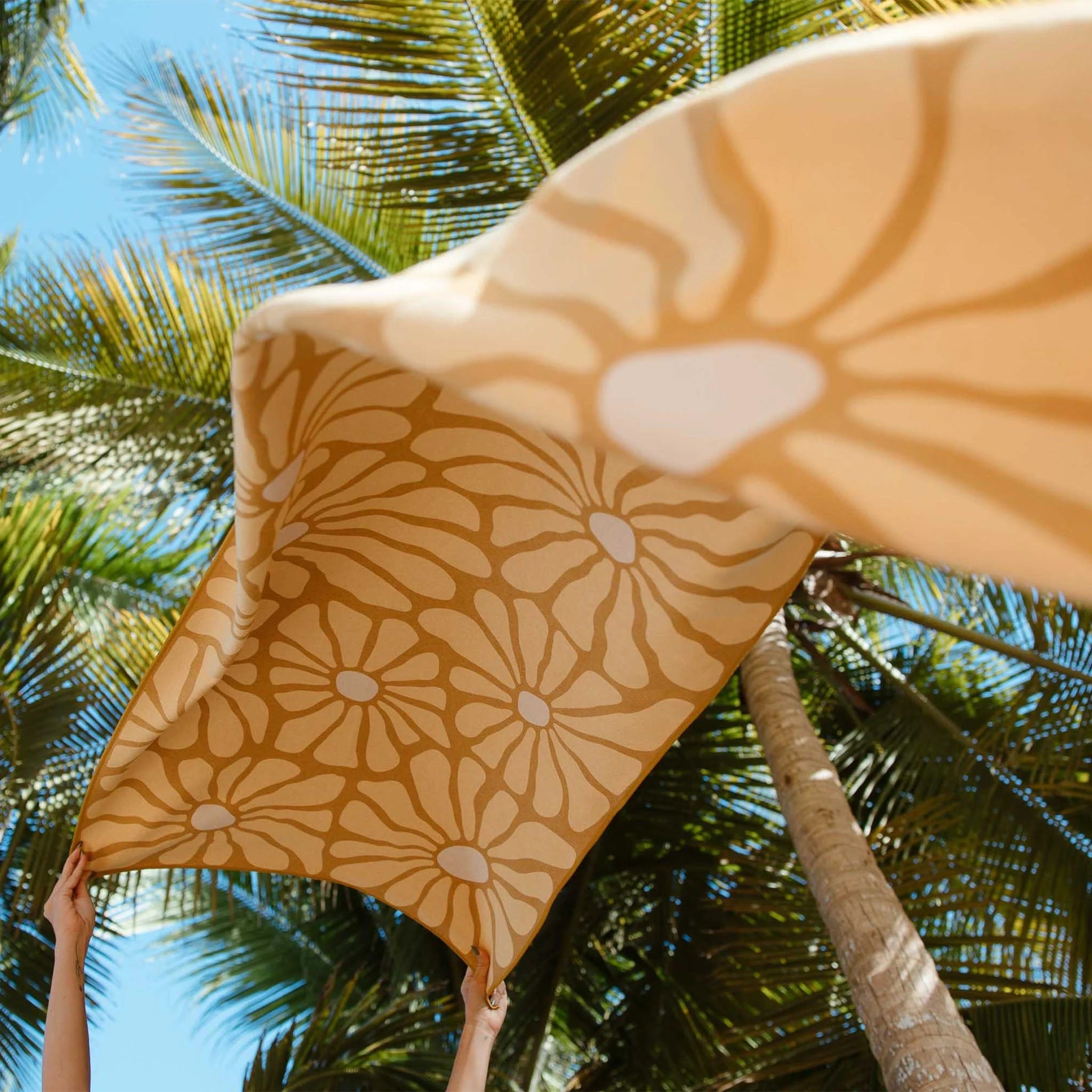 A floral towel blowing in the air with palm trees behind it.