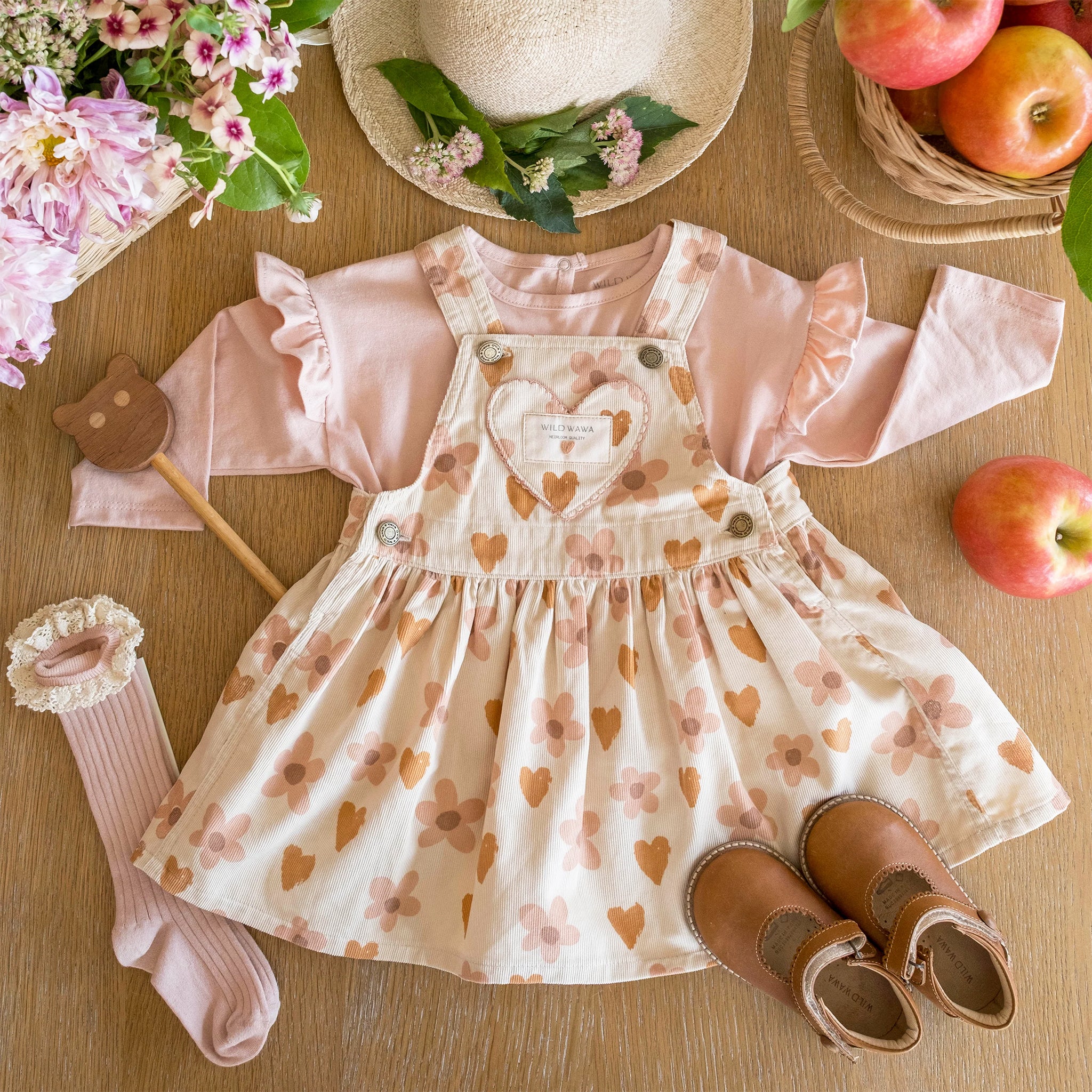 A cream colored overall dress with a burnt orange and pink heart and floral pattern. 