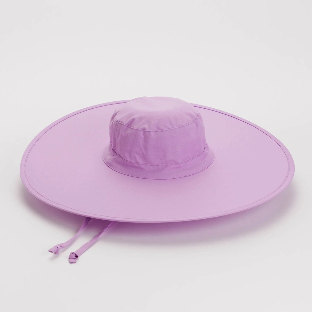 On a white background is a purple nylon sun hat that folds down for easy on the go traveling. It has a wide brim and a neck tie. 