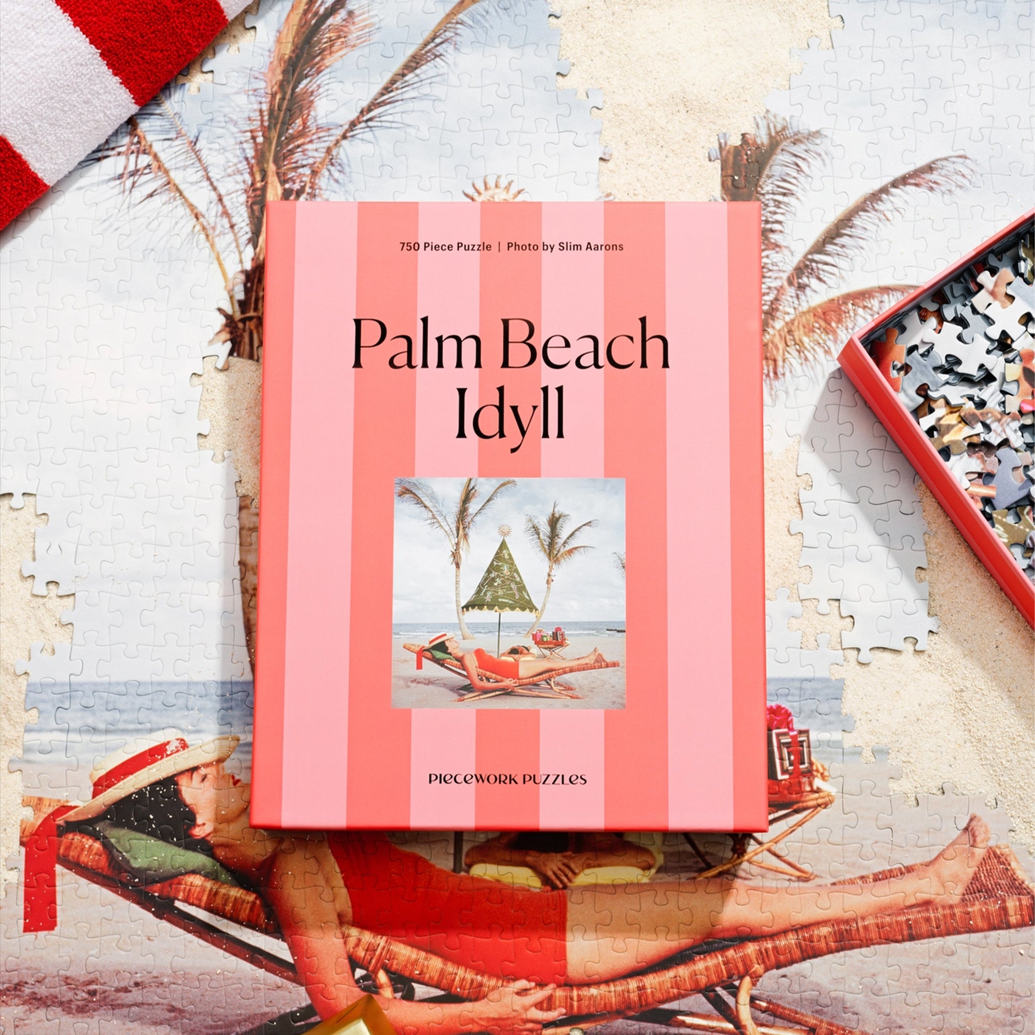 A pink striped boxed puzzle "Palm Beach Idyll" with an image of a retro beach scape. 