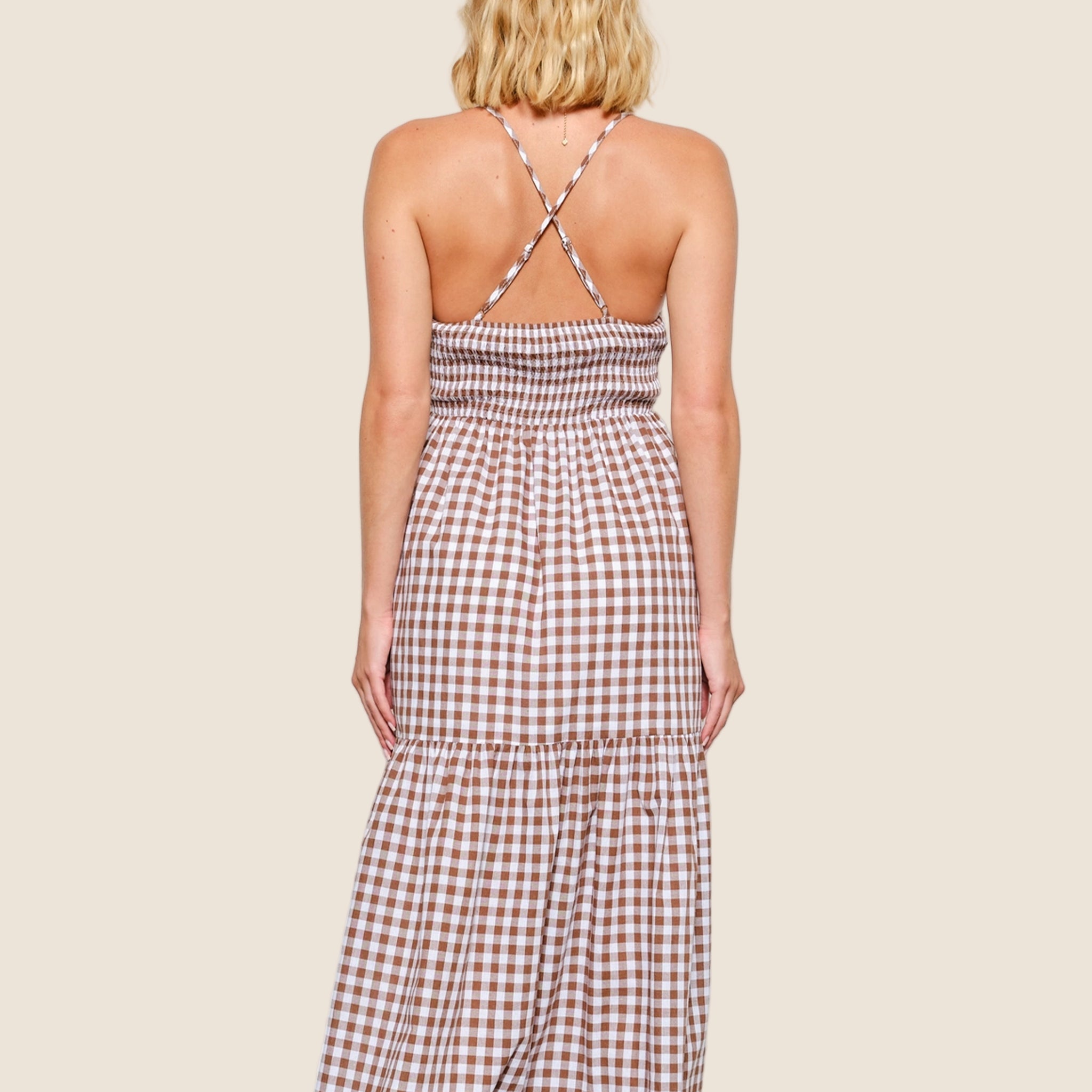 A brown and white gingham dress with spaghetti strap details and a cross back. 