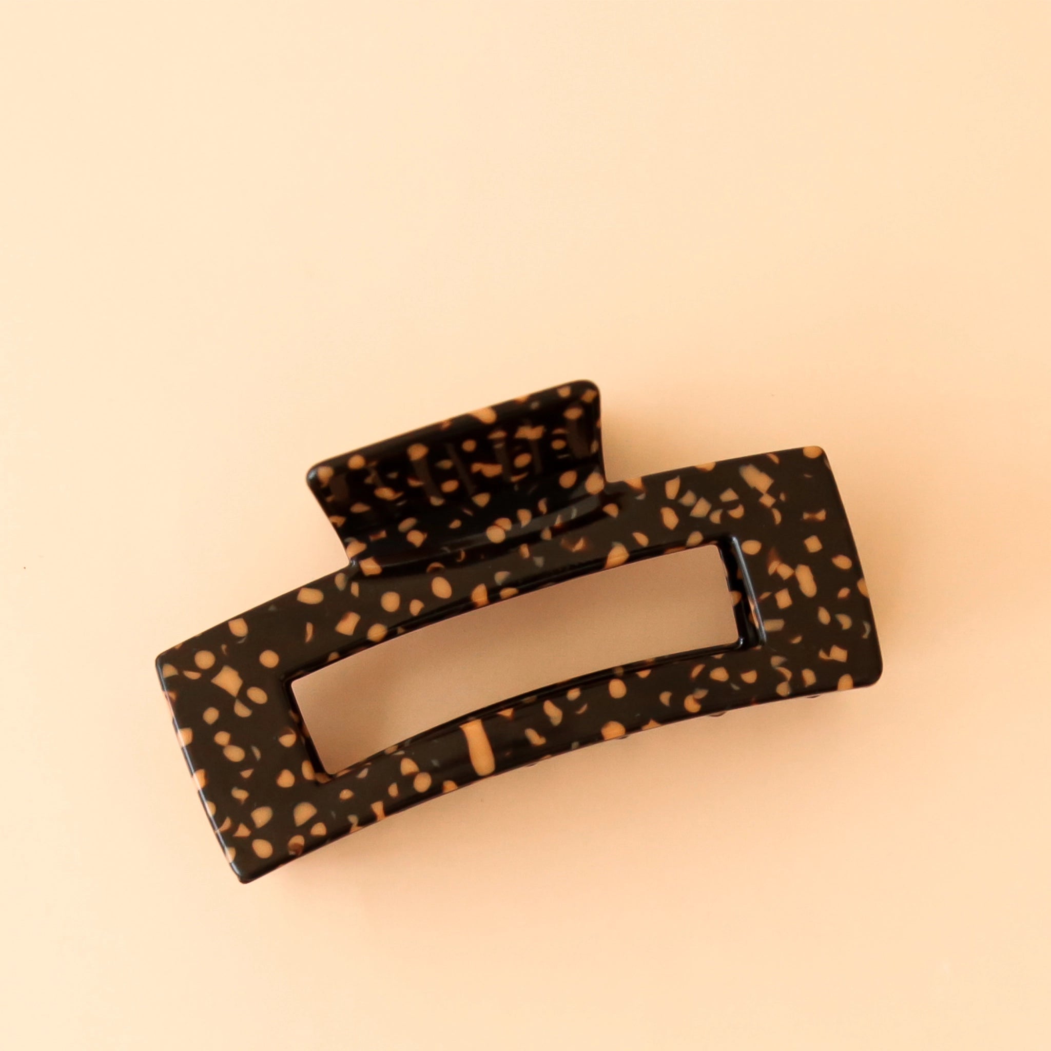 On a peachy background is a dark brown and light orange claw clip in a leopard print. 