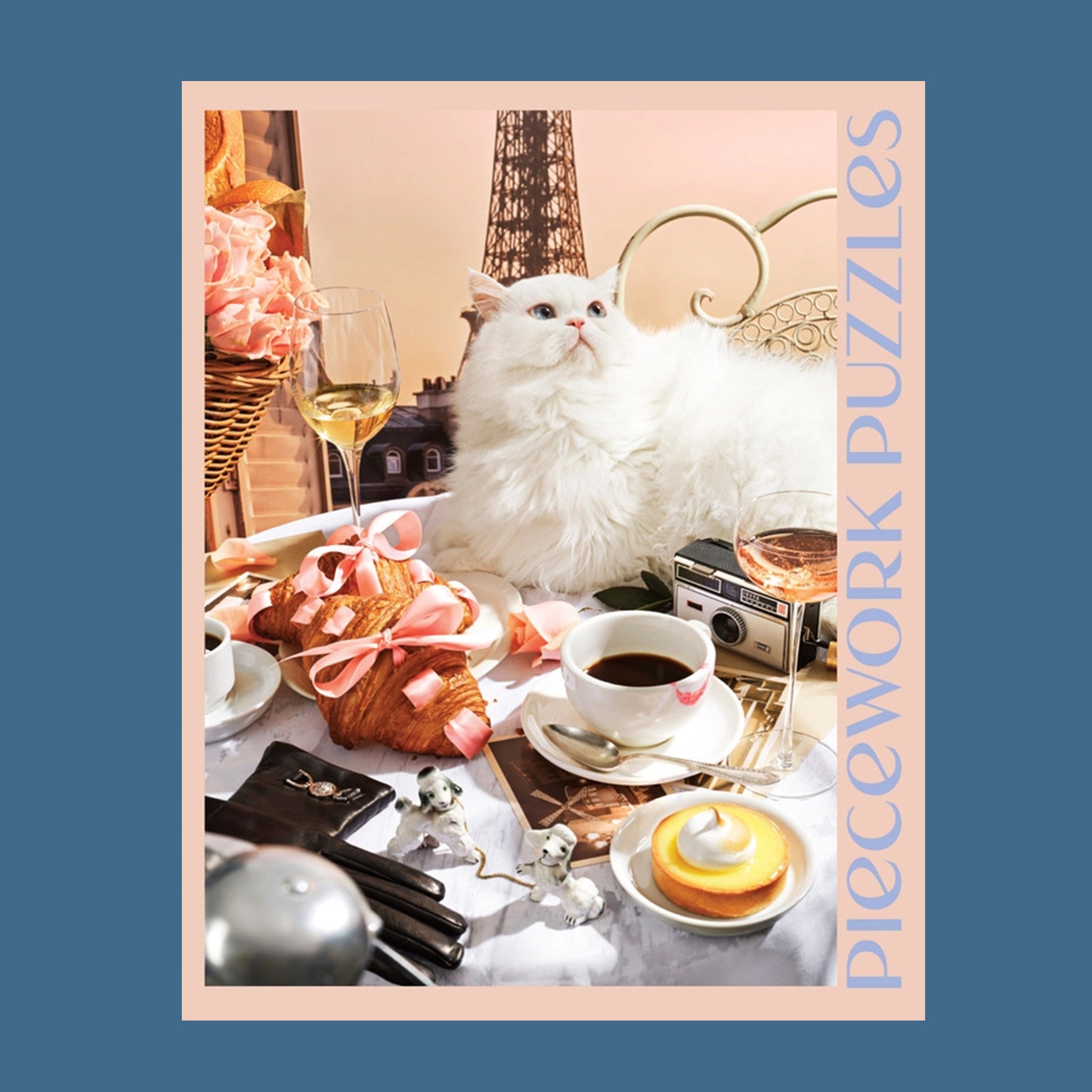 A peachy tan colored puzzle box with a 1000 piece puzzle inside with an image of a white fluffy cat surrounded by French goods such as croissants, macarons, champagne and the Eiffel Tower.