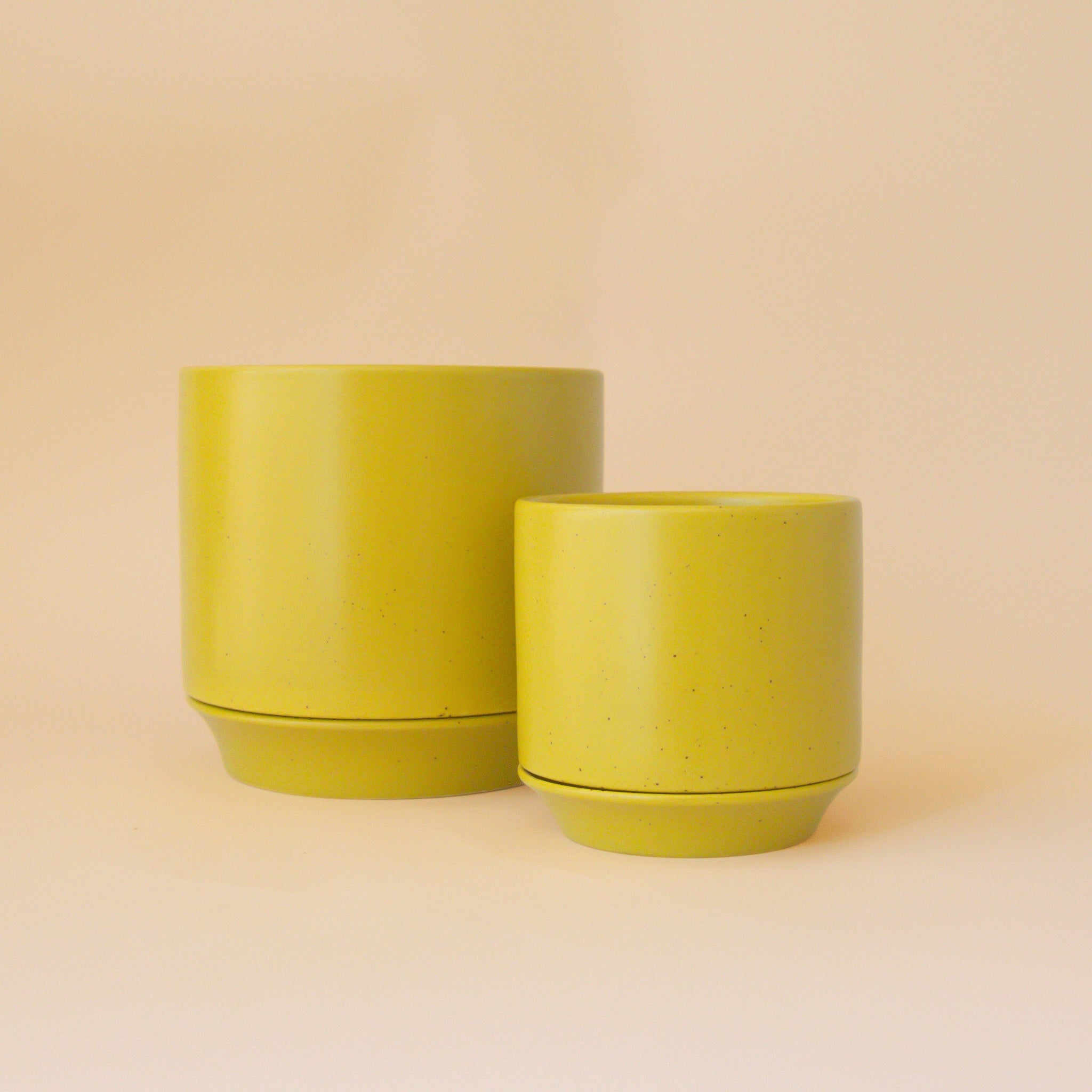 Two beautiful ceramic pots in a yellow-green color sit in middle of image with soft  orange background.
