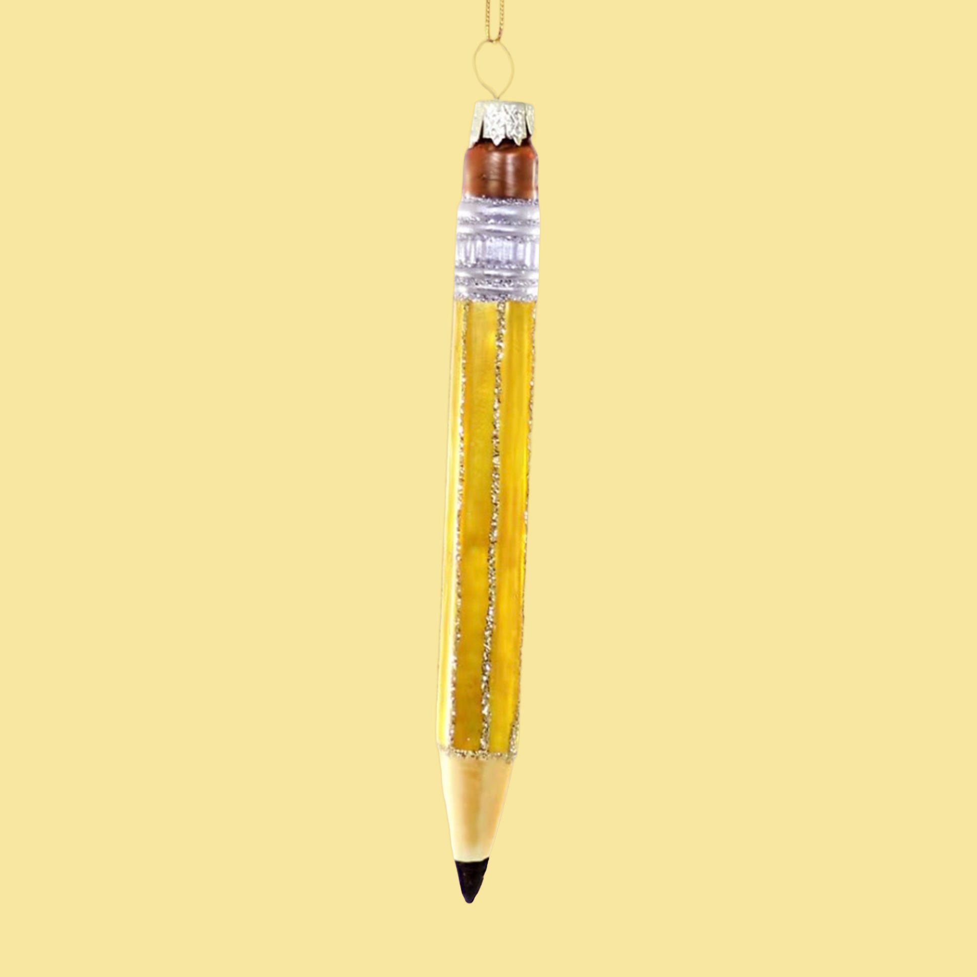 On a yellow ground is a photo of a pencil shaped Christmas ornament. The pencil has a pink eraser, black tip and a gold string hanging at top to hang on a tree.