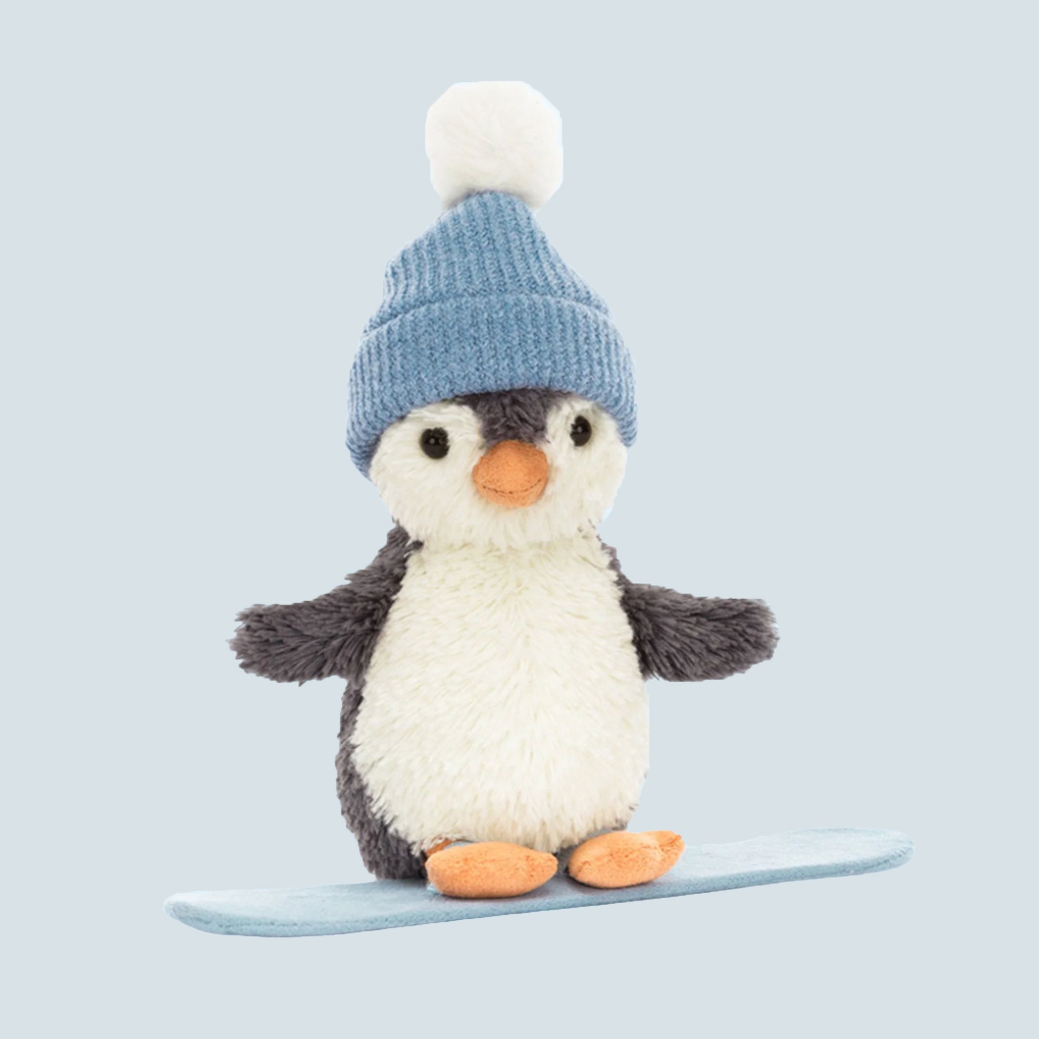 A penguin shaped stuffed animal wearing a beanie and standing on a snowboard. 
