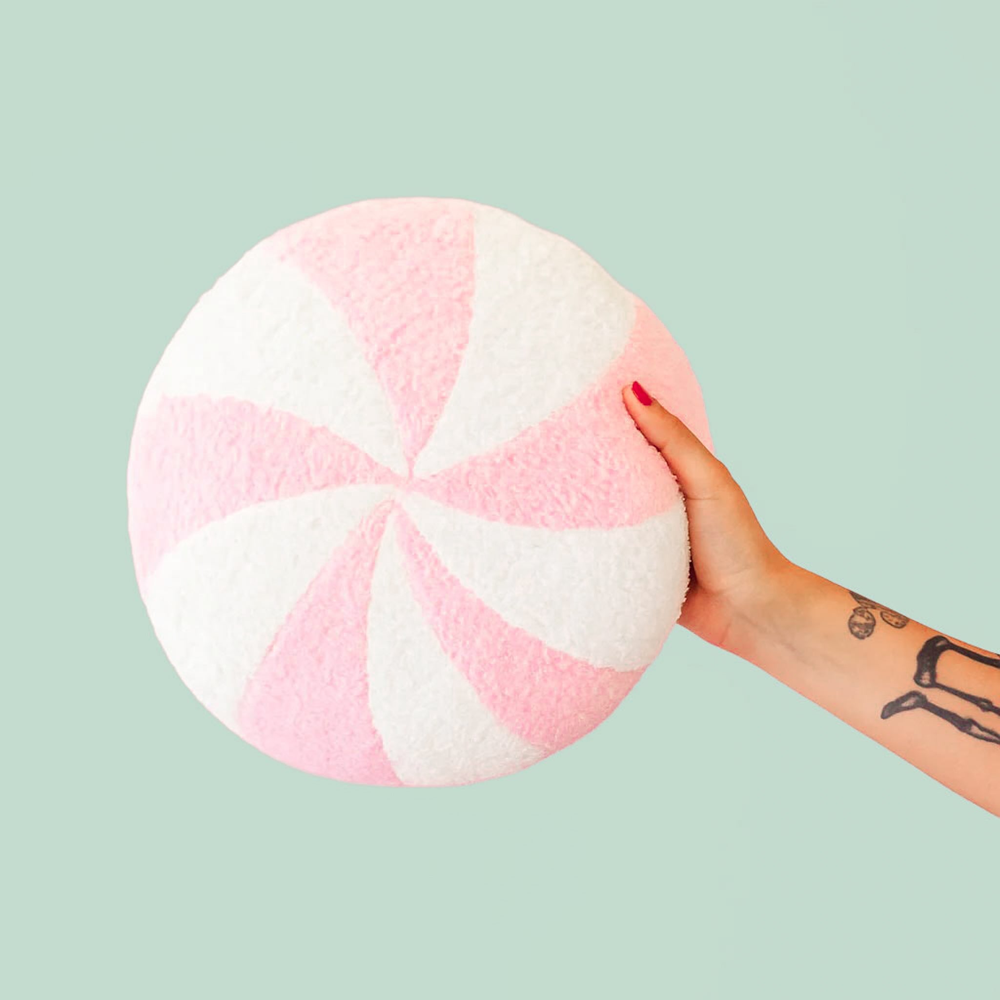 A round pink and white peppermint swirl candy shaped throw pillow. 