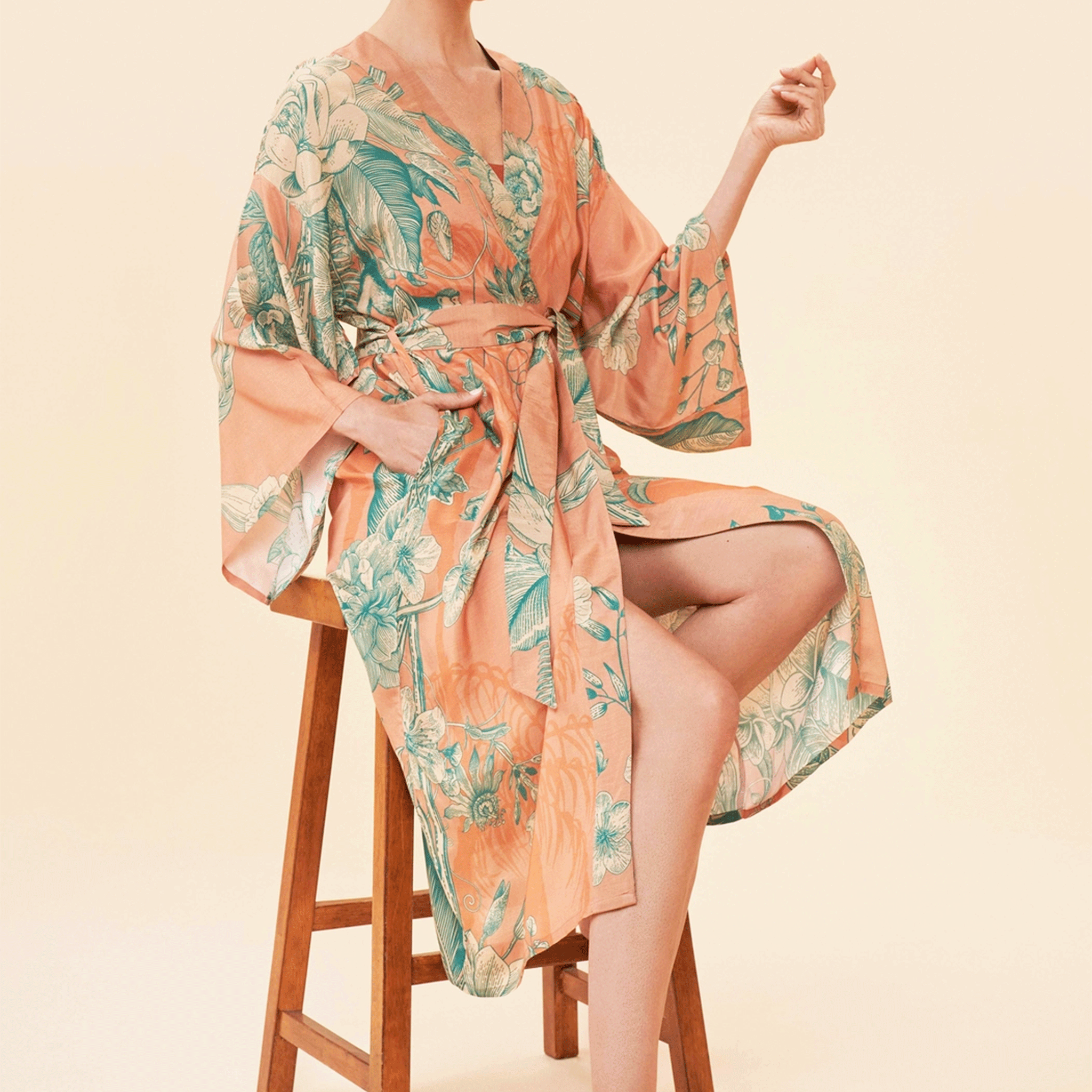 On a tan background is a model wearing an orange and teal kimono robe.