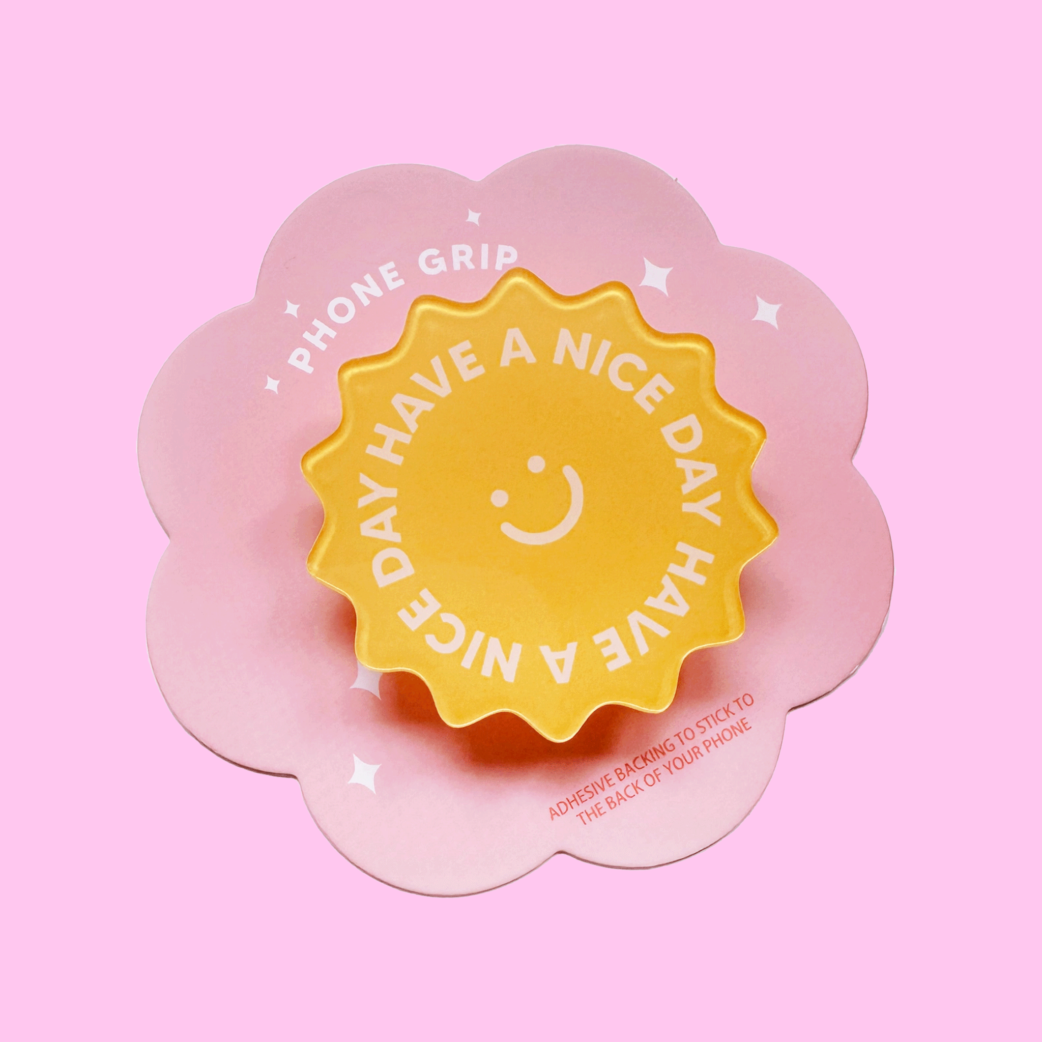 On a pink background is a yellow sun shaped phone grip with text on it that reads, "Have A Nice Day Have A Nice Day".