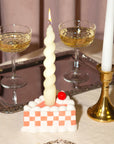 A pink and white checkered piece of cake candle holder with a hole in the center for the taper candle. Taper candles not included with purchase. 