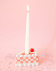 A pink and white checkered piece of cake candle holder with a hole in the center for the taper candle. Taper candles not included with purchase. 