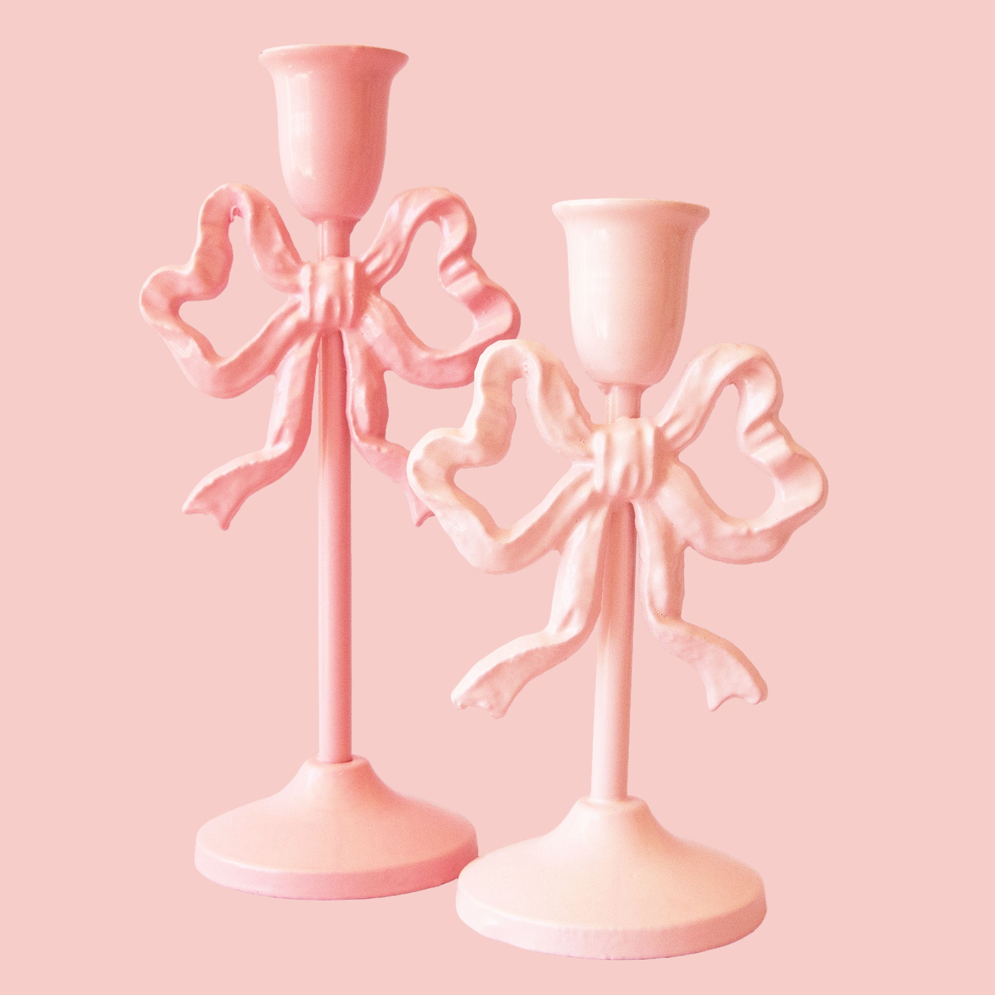 Two bow-shaped metal candle stick holders in shades of pink.