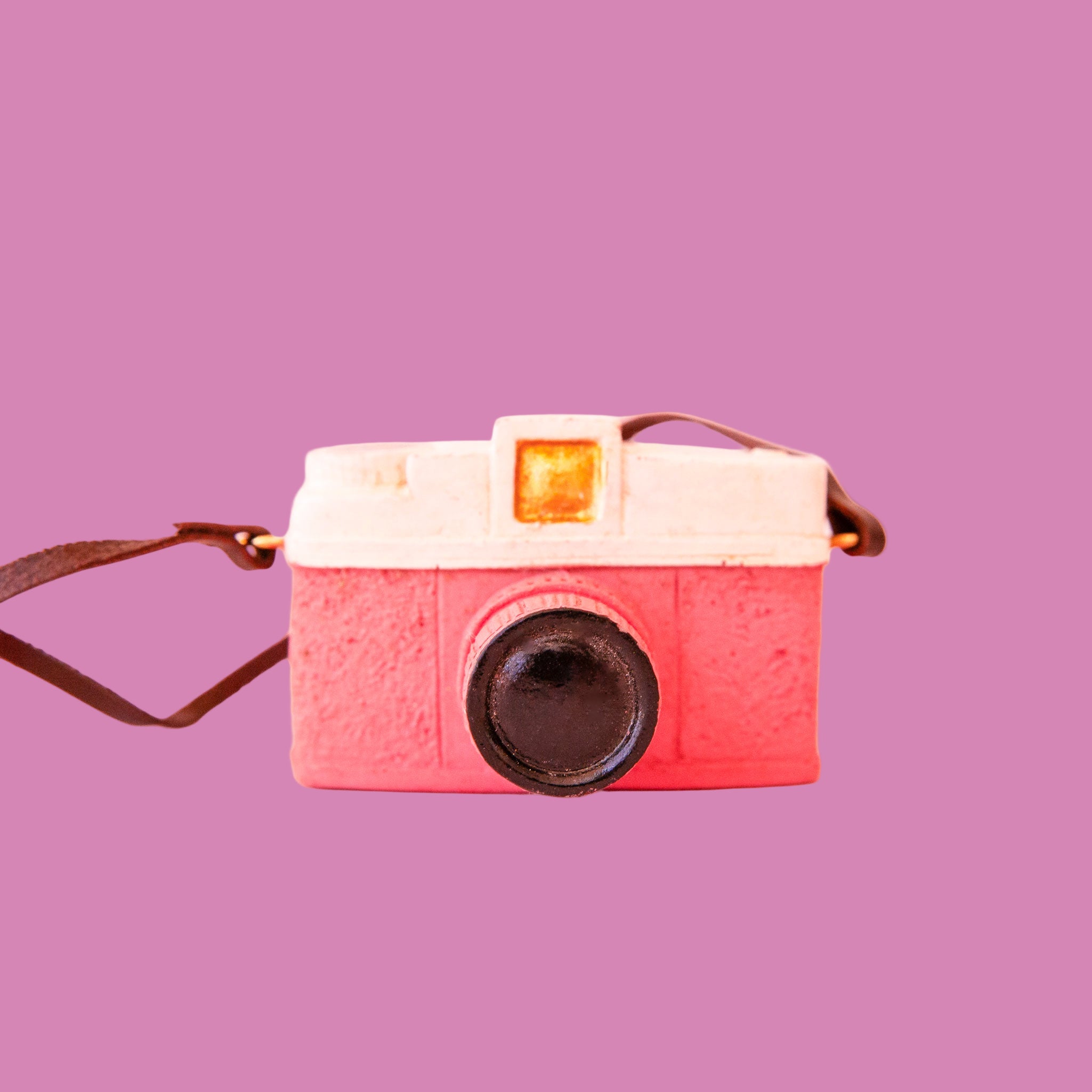 Pink camera ornament with white and gold details and a leather strap. 