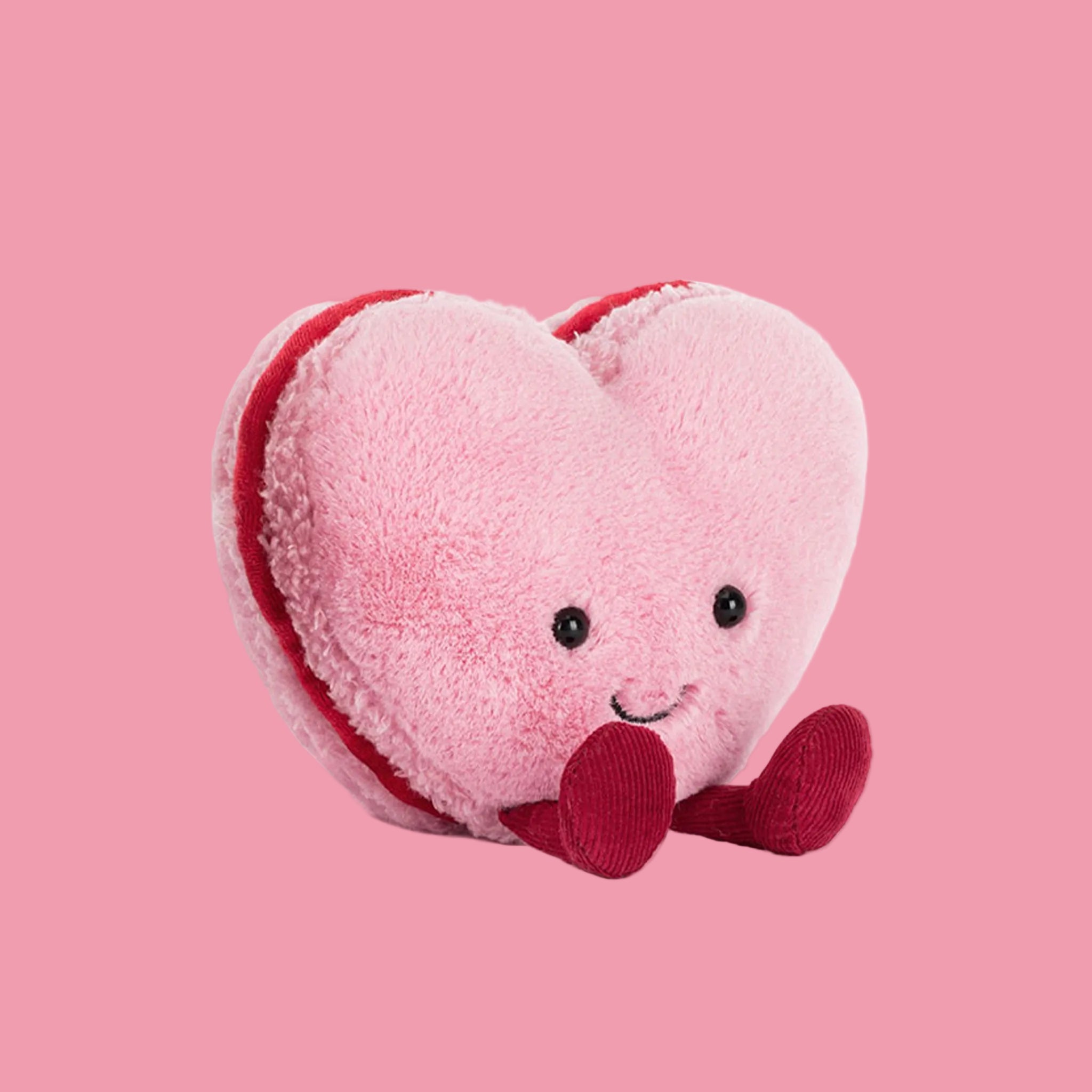 A heart shaped macaron stuffed toy with a smiling face. 