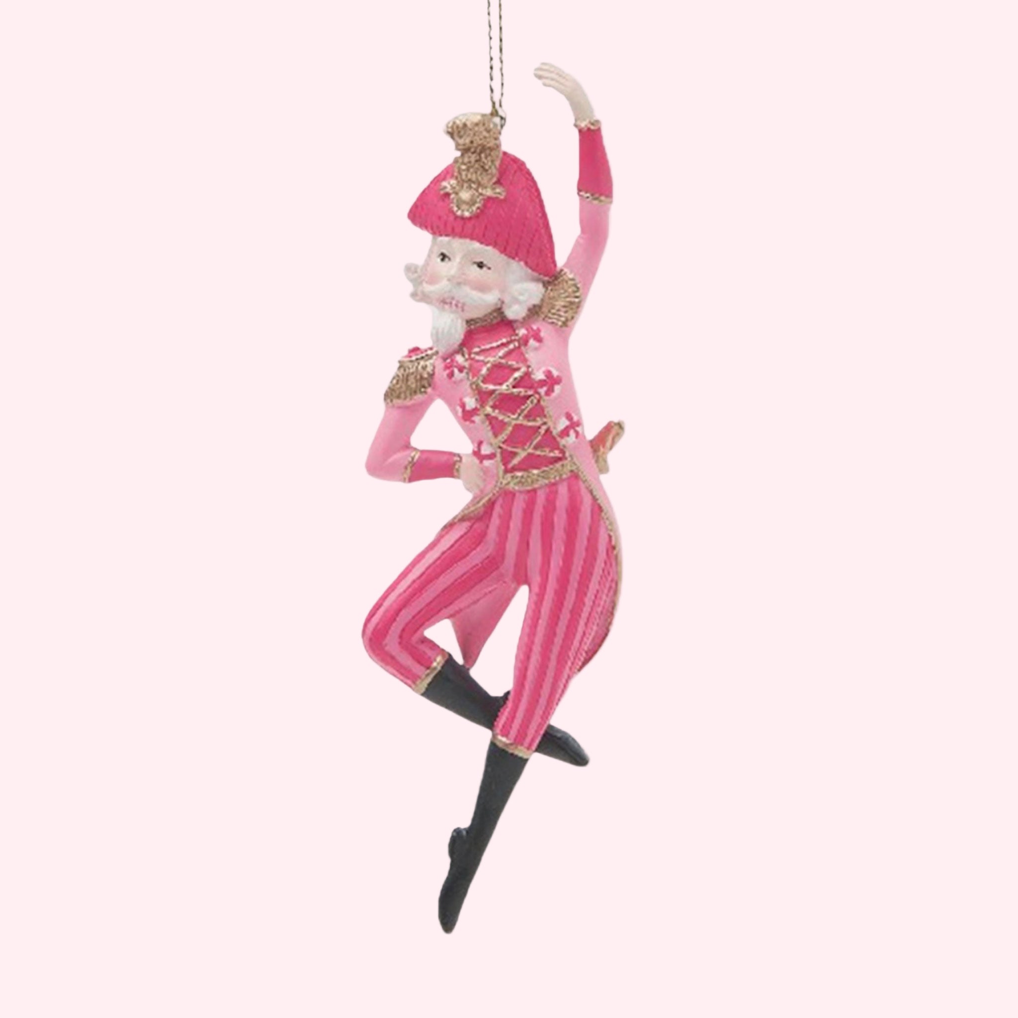 A pink nutcracker ornament dancing on a pink background.