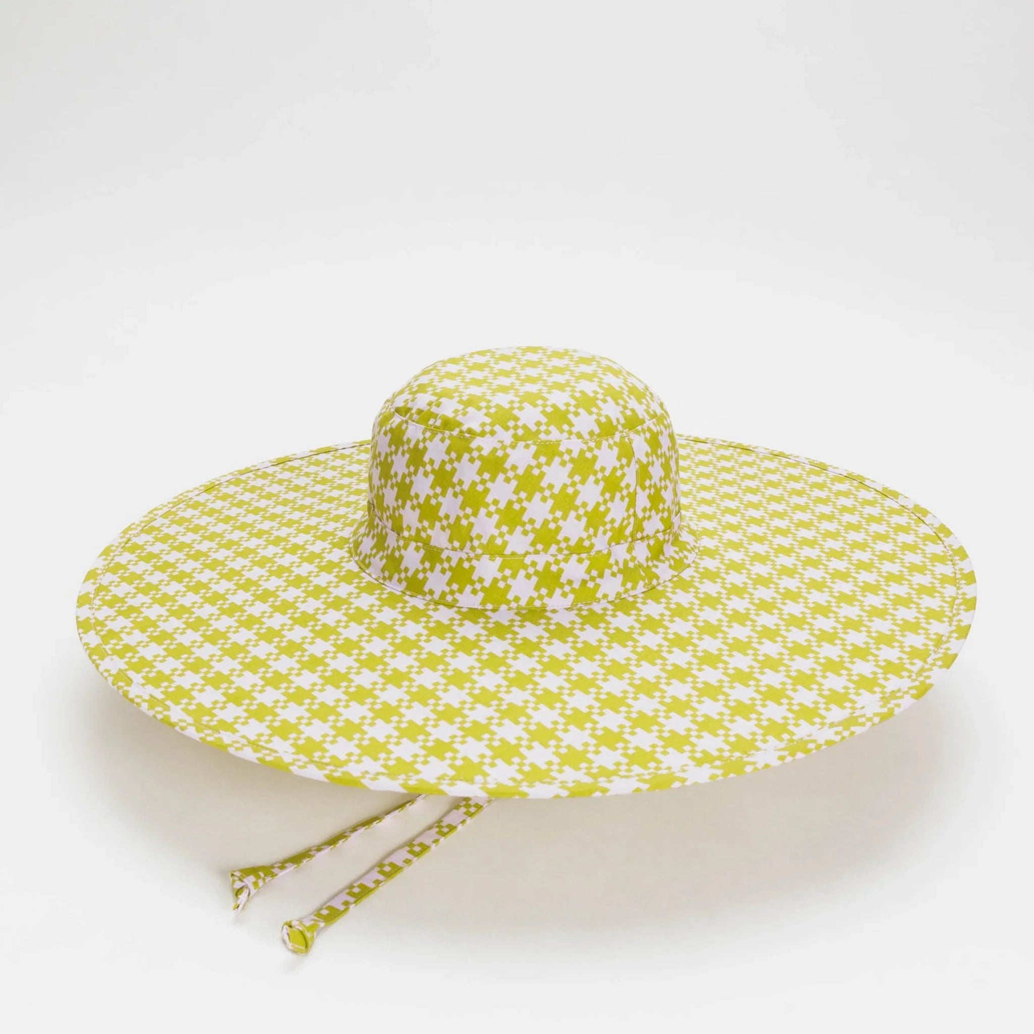 On a light grey background is a green and light pink gingham printed hat with a wide brim and features a nylon material that can fold up for easy traveling. 