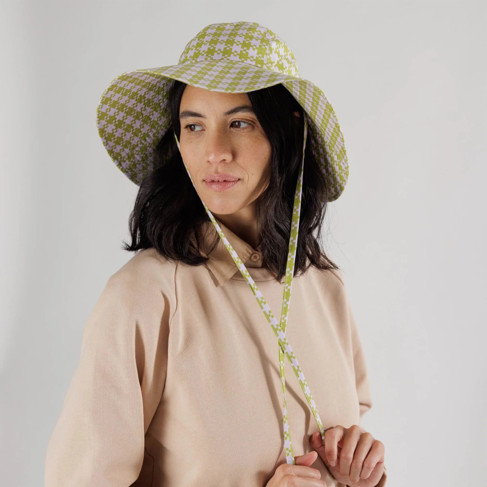 On a white background is a pink and green flexible sun hat with to straps for securing around the neck. 