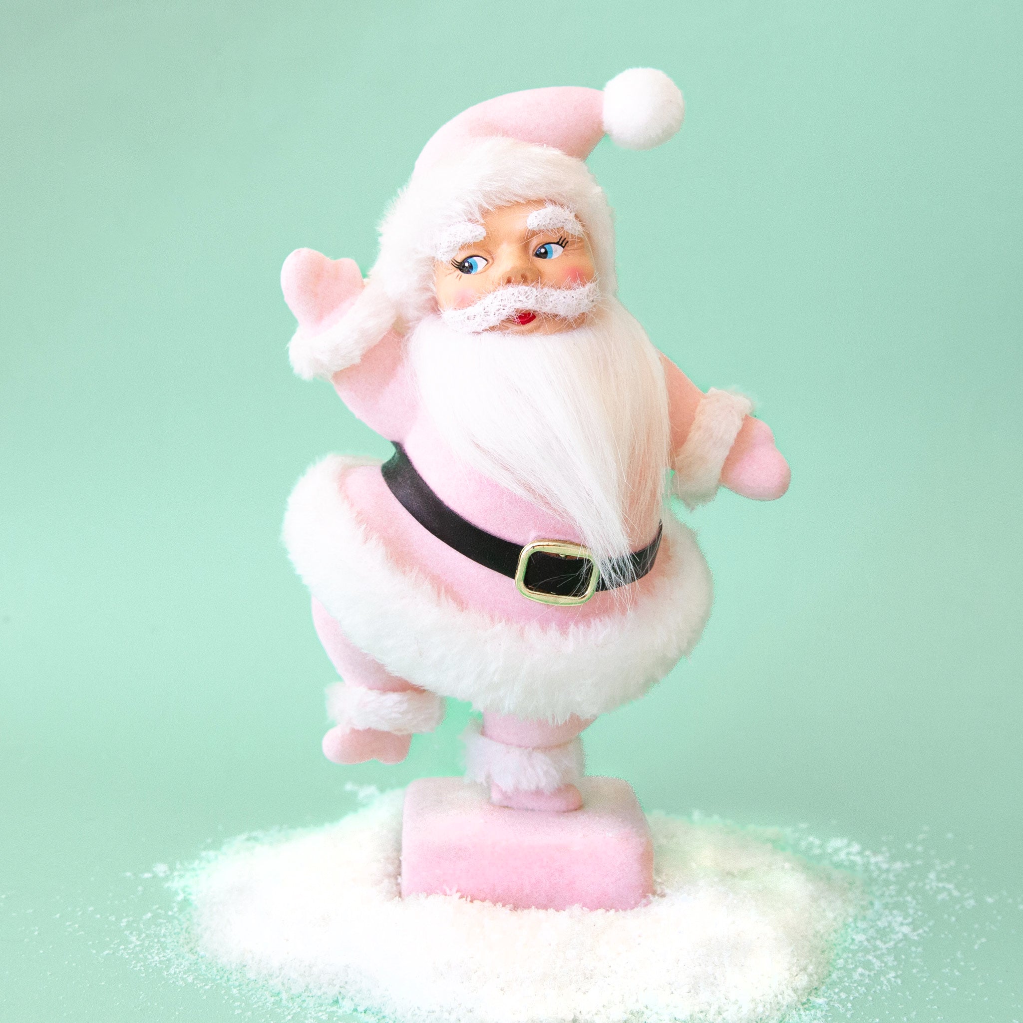 On a mint background is a Santa figurine with a pink flocked suit and white furry details. 