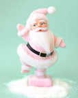 On a mint background is a Santa figurine with a pink flocked suit and white furry details. 