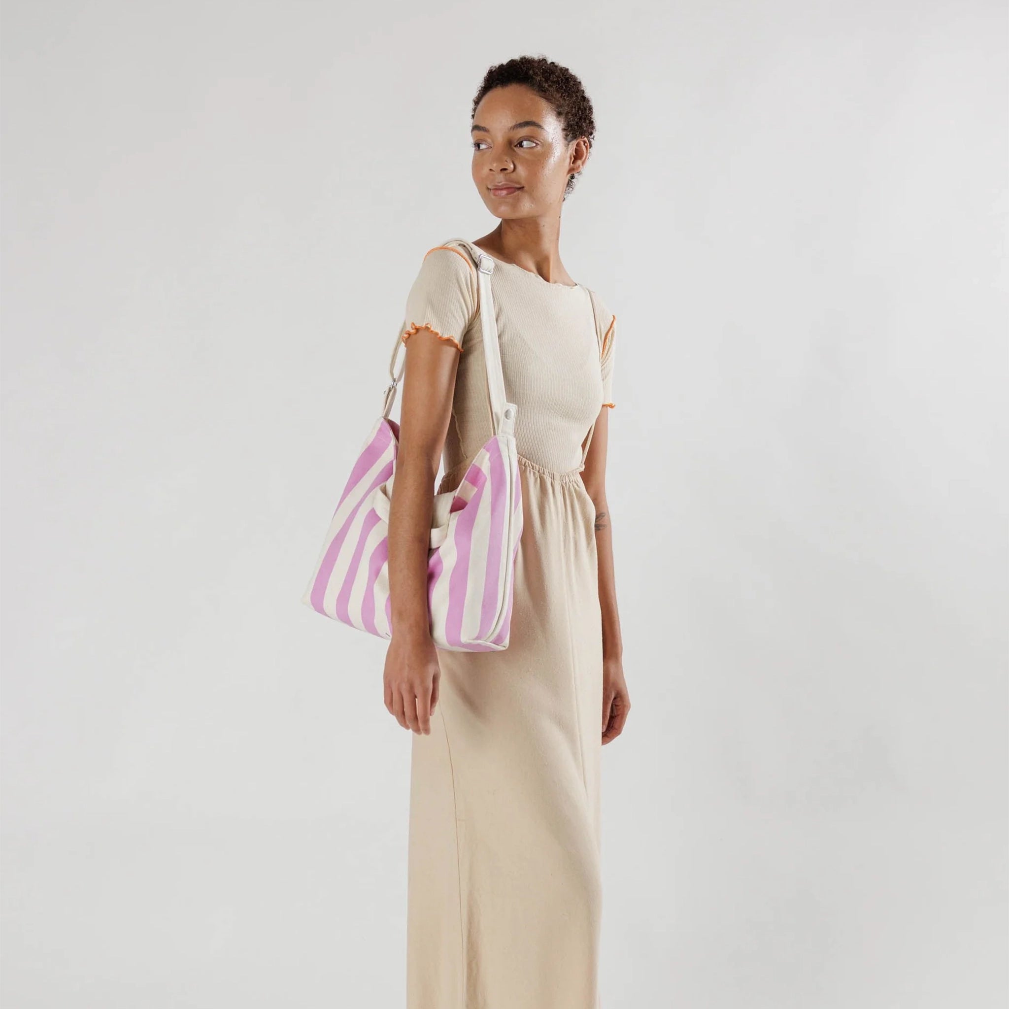 On a white background is a square tote bag with white and hot pink stripes along with two handles and a longer crossbody or shoulder strap.