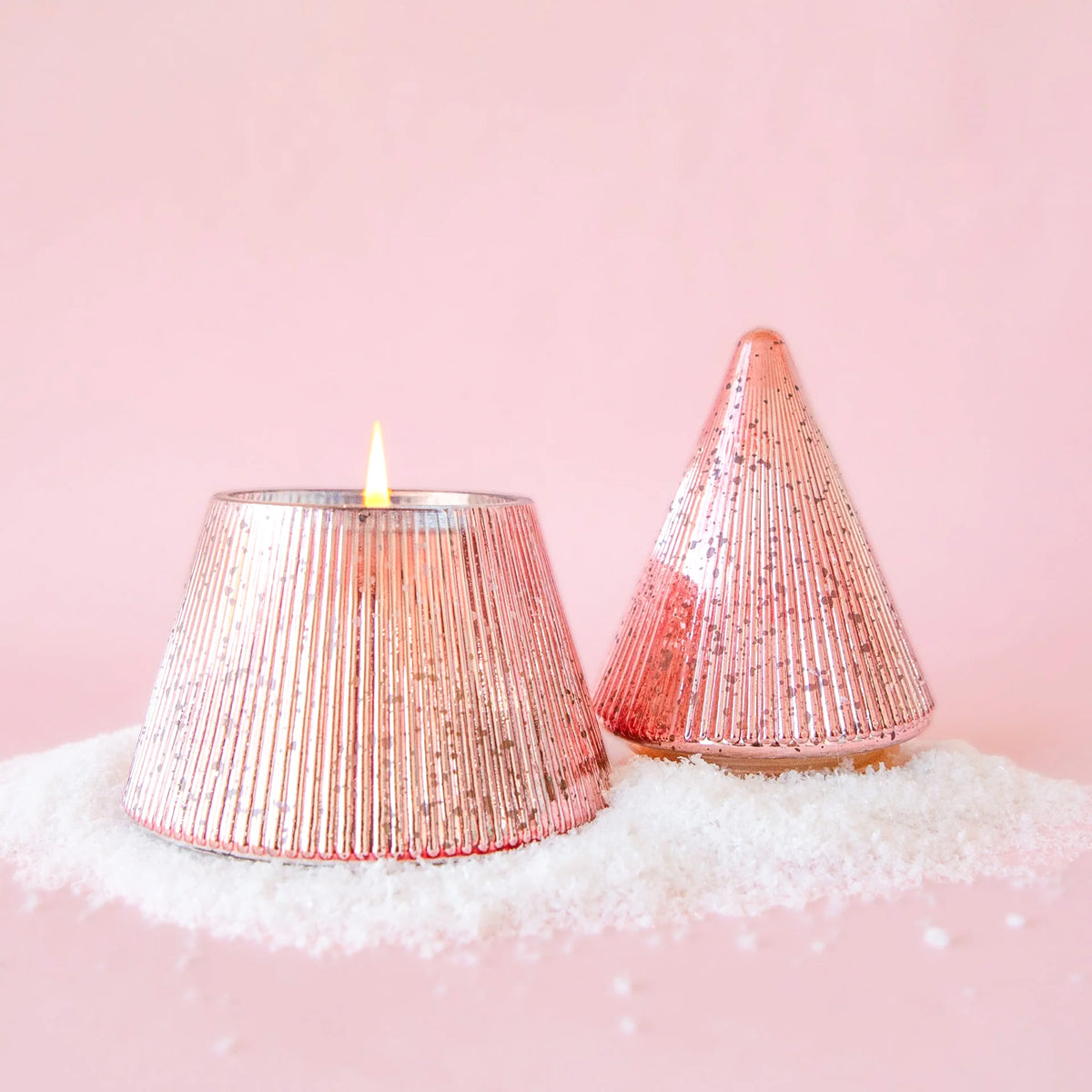 Pink Christmas tree shaped candle with mercury glass detail.  The candle has a lit flame and sits on a bed of fake snow.