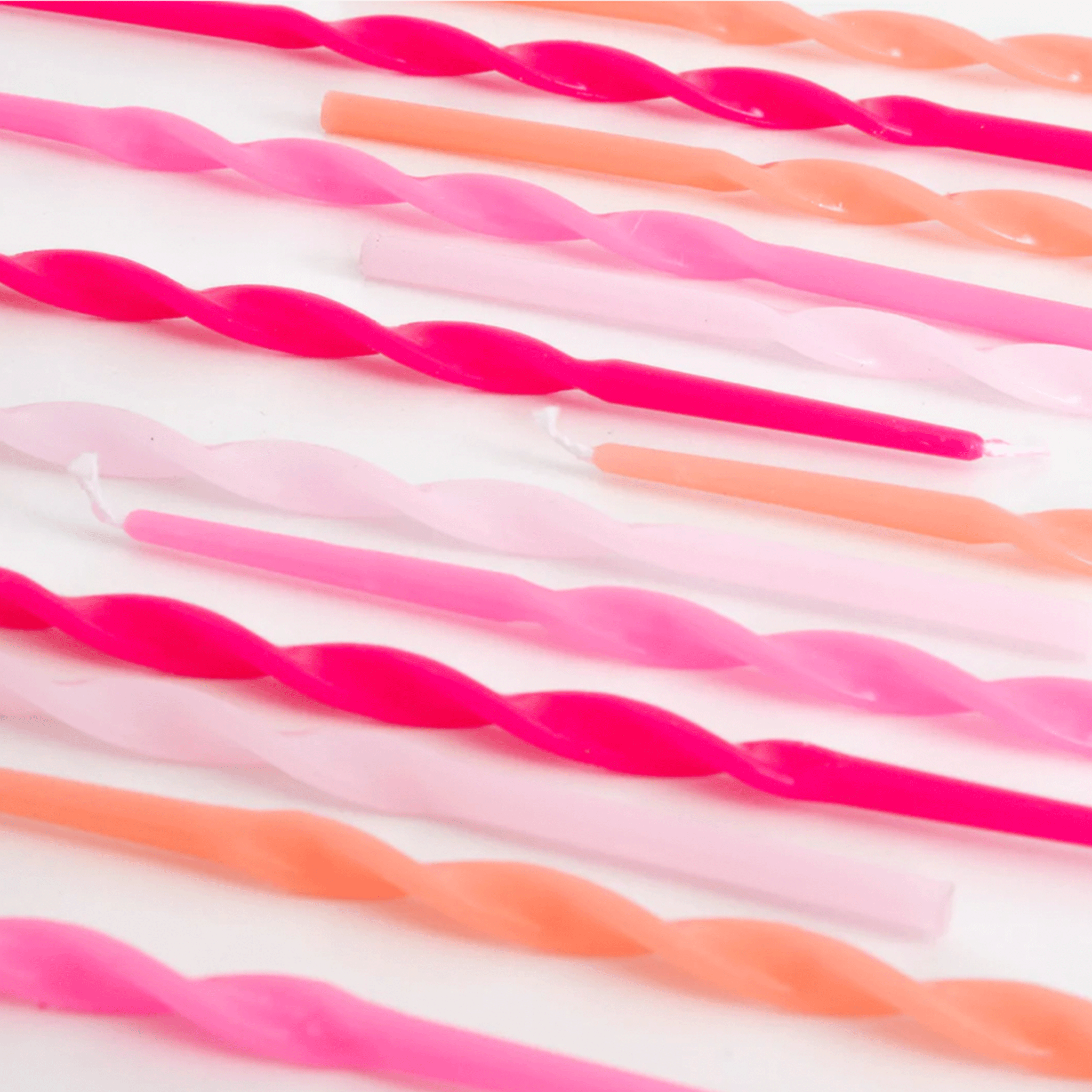 On a white background is a variety of long pink twisted candles. 