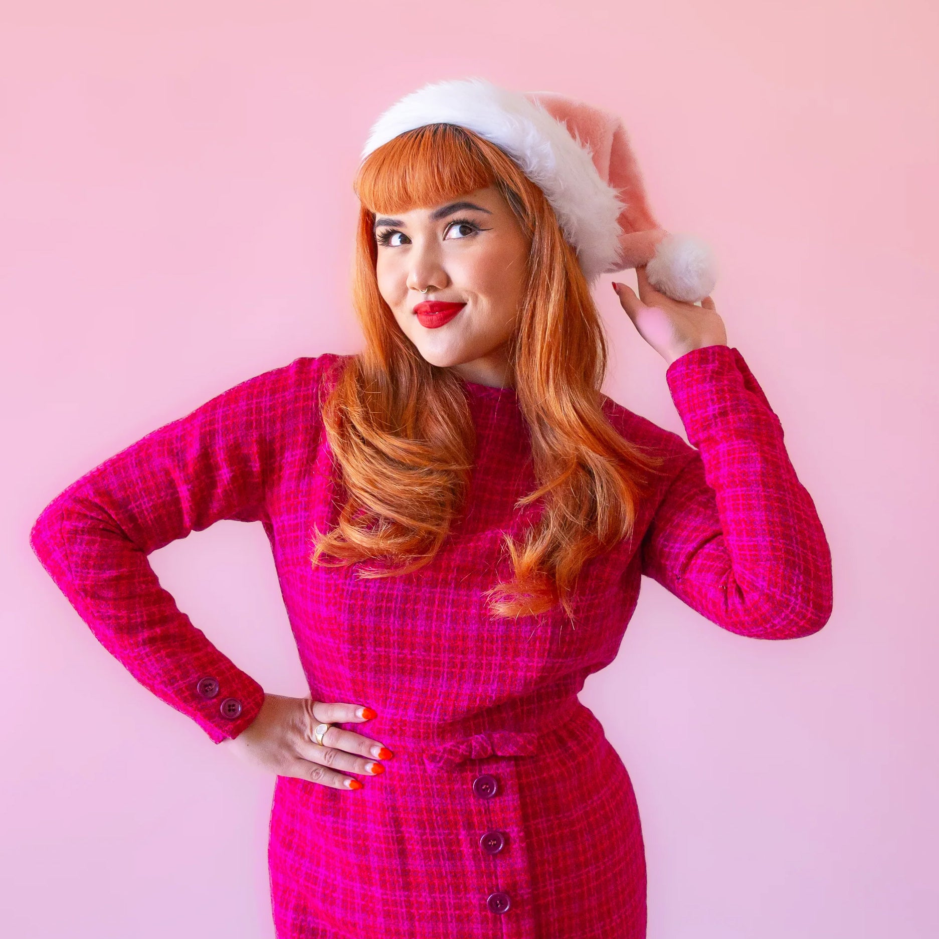 On a pink background is a model wearing pink santa hat with white faux fur detailing.